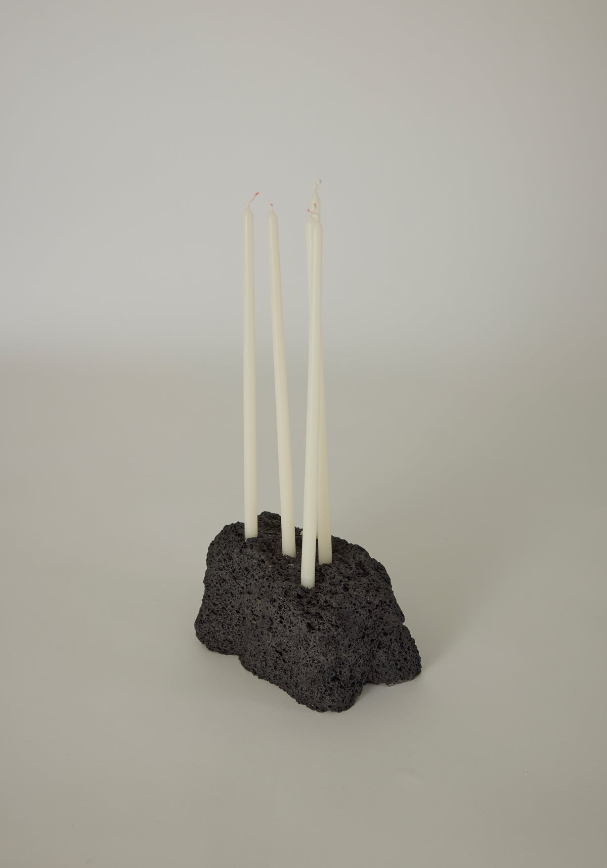 Sculptural Stone Candle Holder featuring four white taper candles in a handcrafted, porous black lava stone base by Dutch artist Louis Crombag.