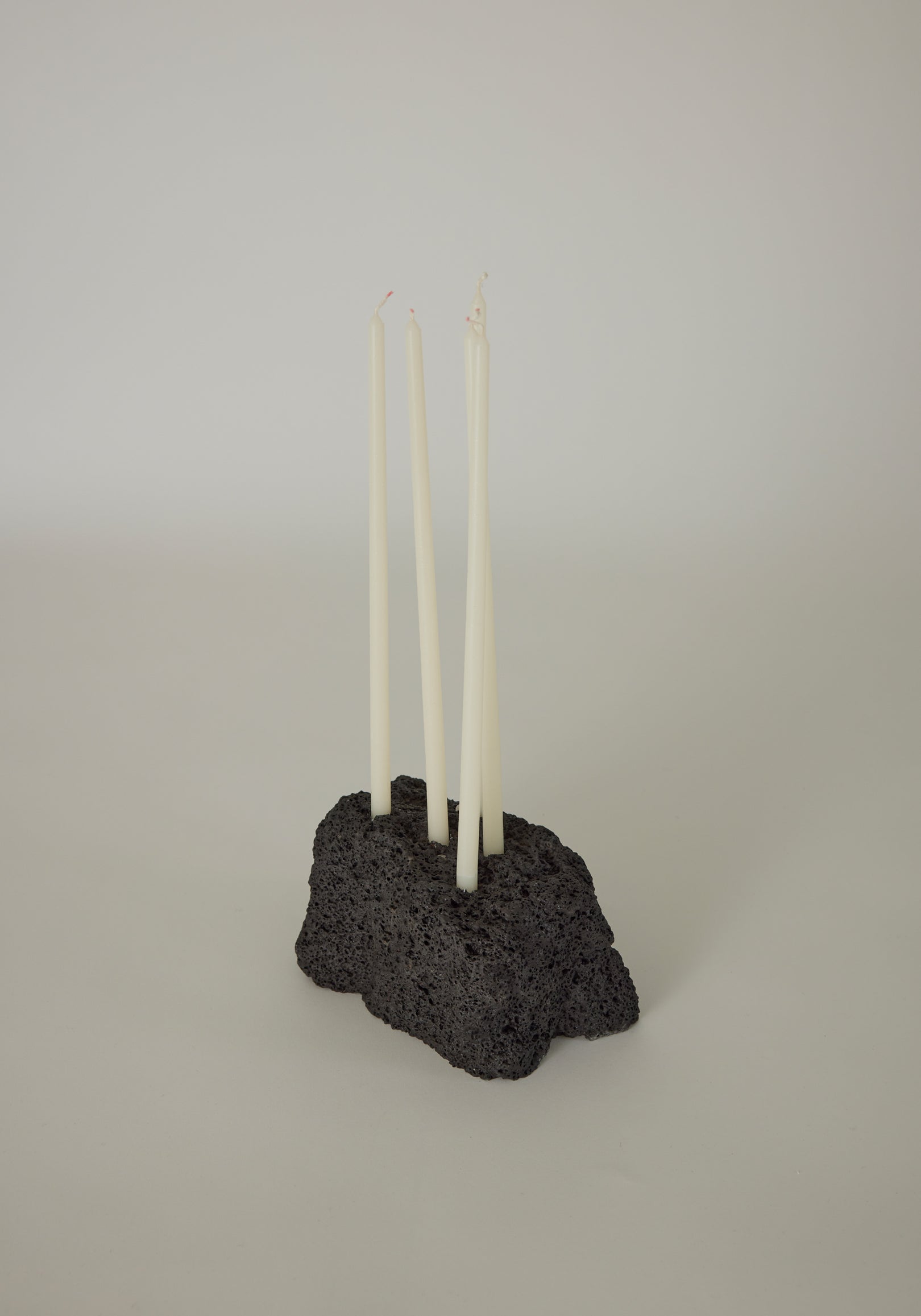 Sculptural Stone Candle Holder featuring four white taper candles in a handcrafted, porous black lava stone base by Dutch artist Louis Crombag.