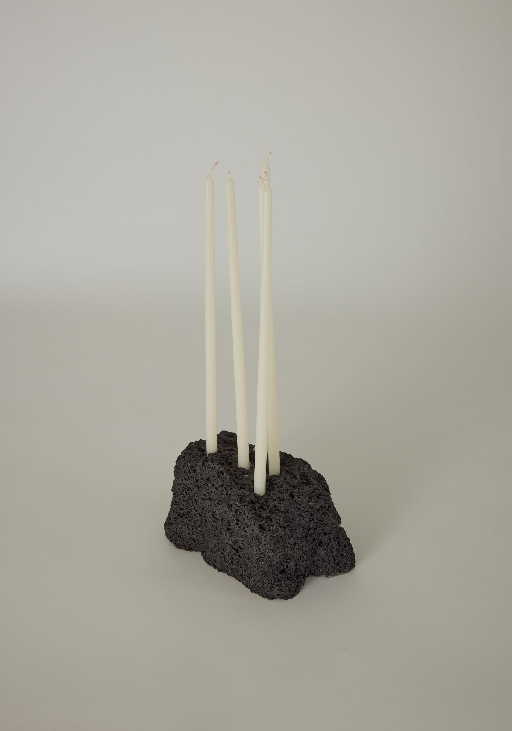 Sculptural Stone Candle Holder featuring four white taper candles in a handcrafted, porous black lava stone base by Dutch artist Louis Crombag.
