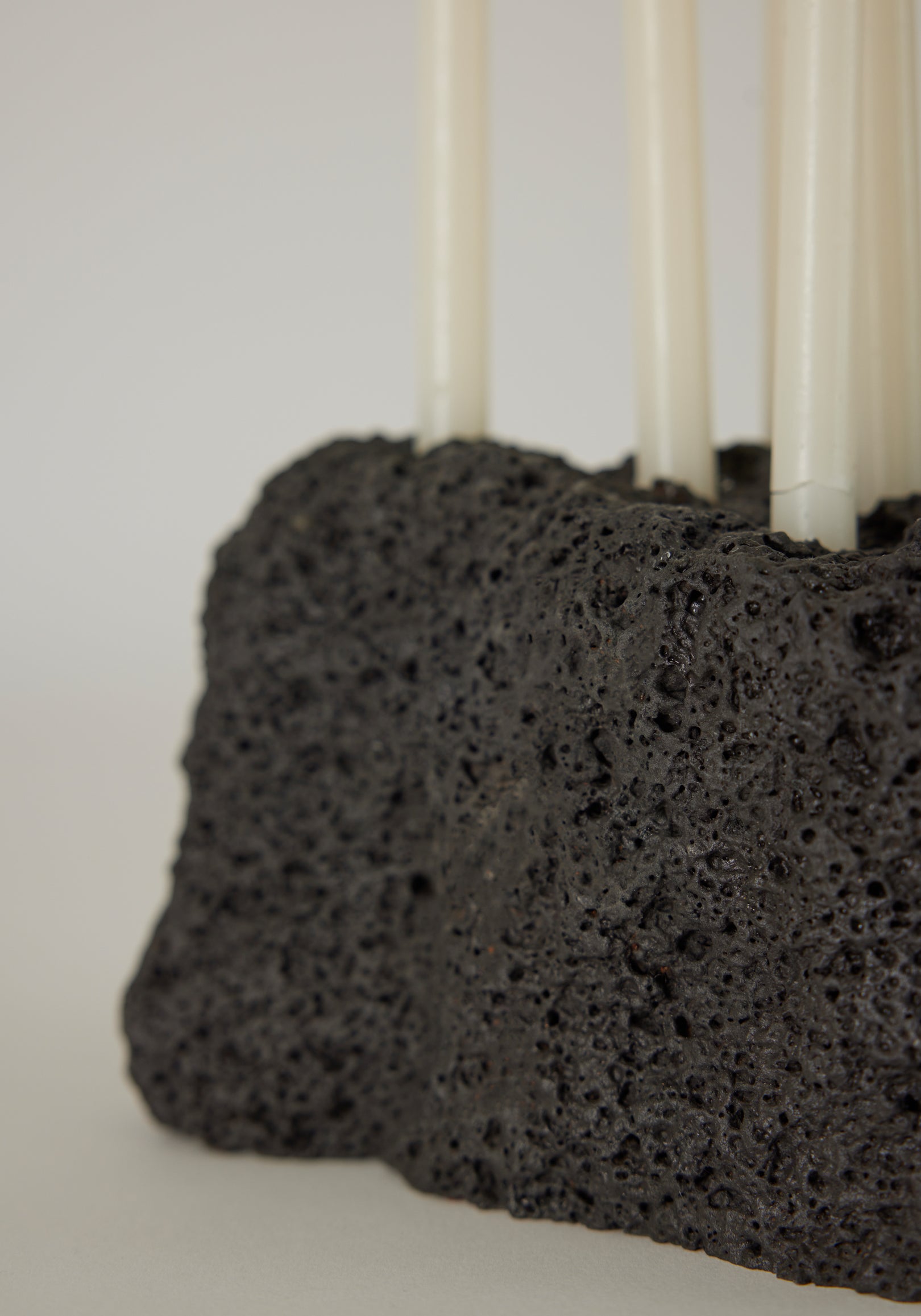 Sculptural Stone Candle Holder made from porous black lava stone, featuring six slender white taper candles, handcrafted by Dutch artist Louis Crombag.