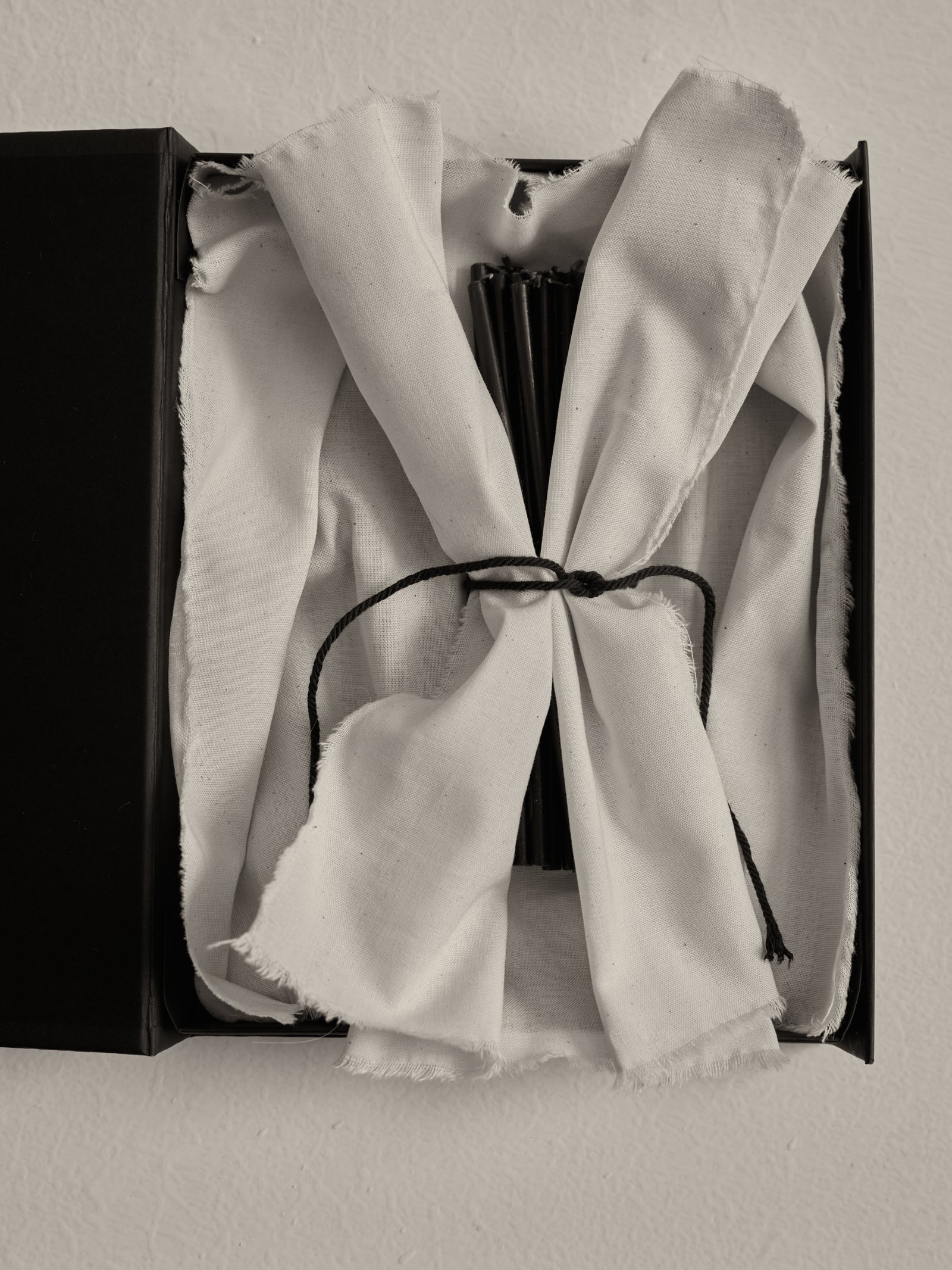 Candles 5mm | noir: Partially opened box revealing off-white cloth with slender black candles, 100% beeswax. Perfect for travertine objects, 0.5-hour burn time each.