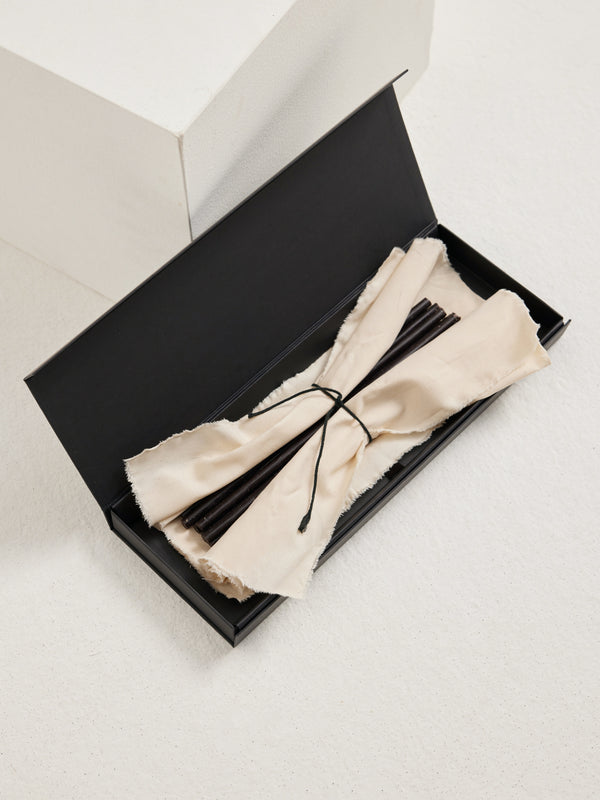 Candles 10mm | noir: Matte-black box with off-white cloth reveals slender incense-like sticks, actually beeswax candles, 30.5cm tall, fitting 10mm holders.