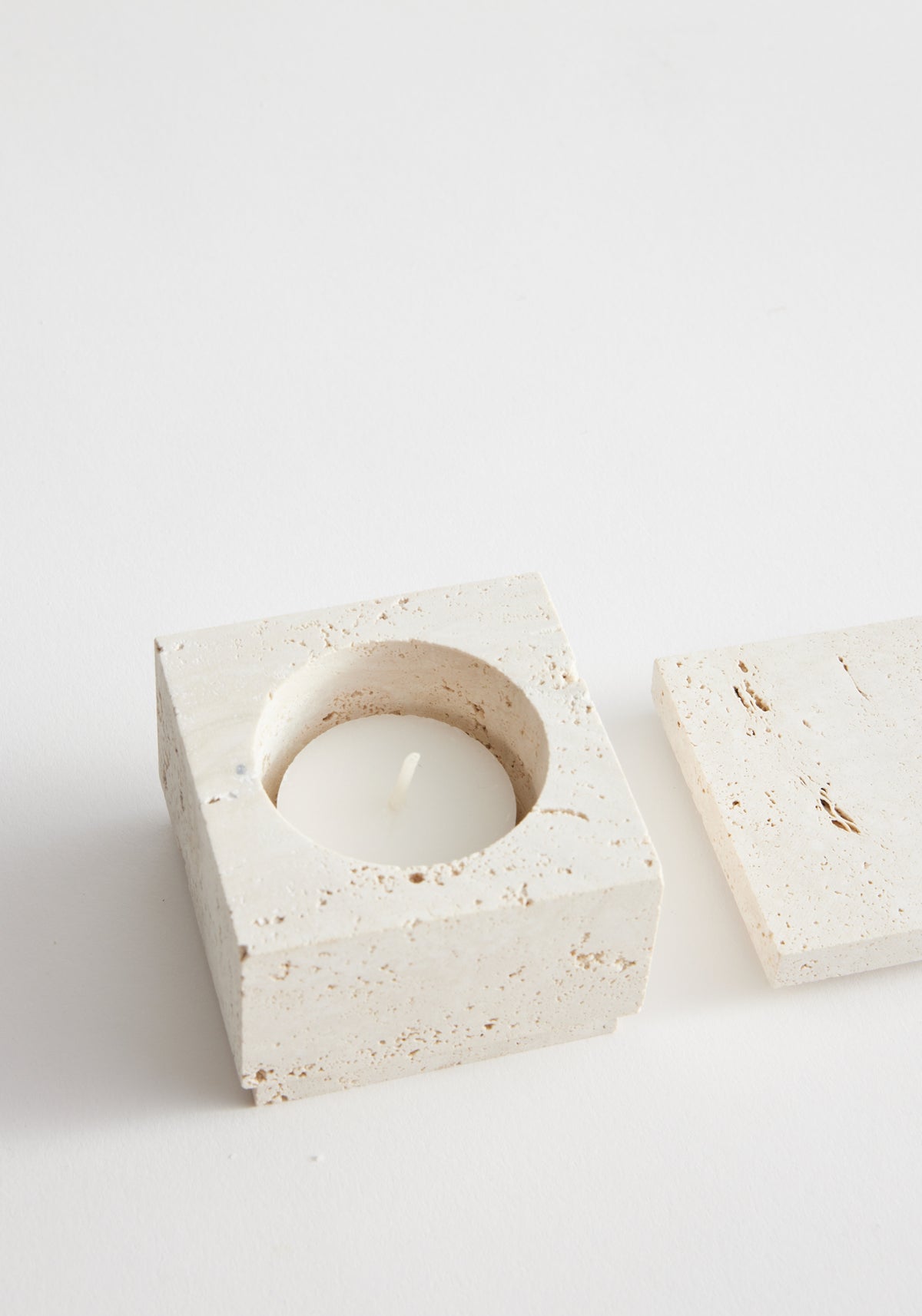 Tealight box | travertine: A small, square travertine container with a hollow center for a tealight, accompanied by a matching lid. Handcrafted by Louis Crombag.