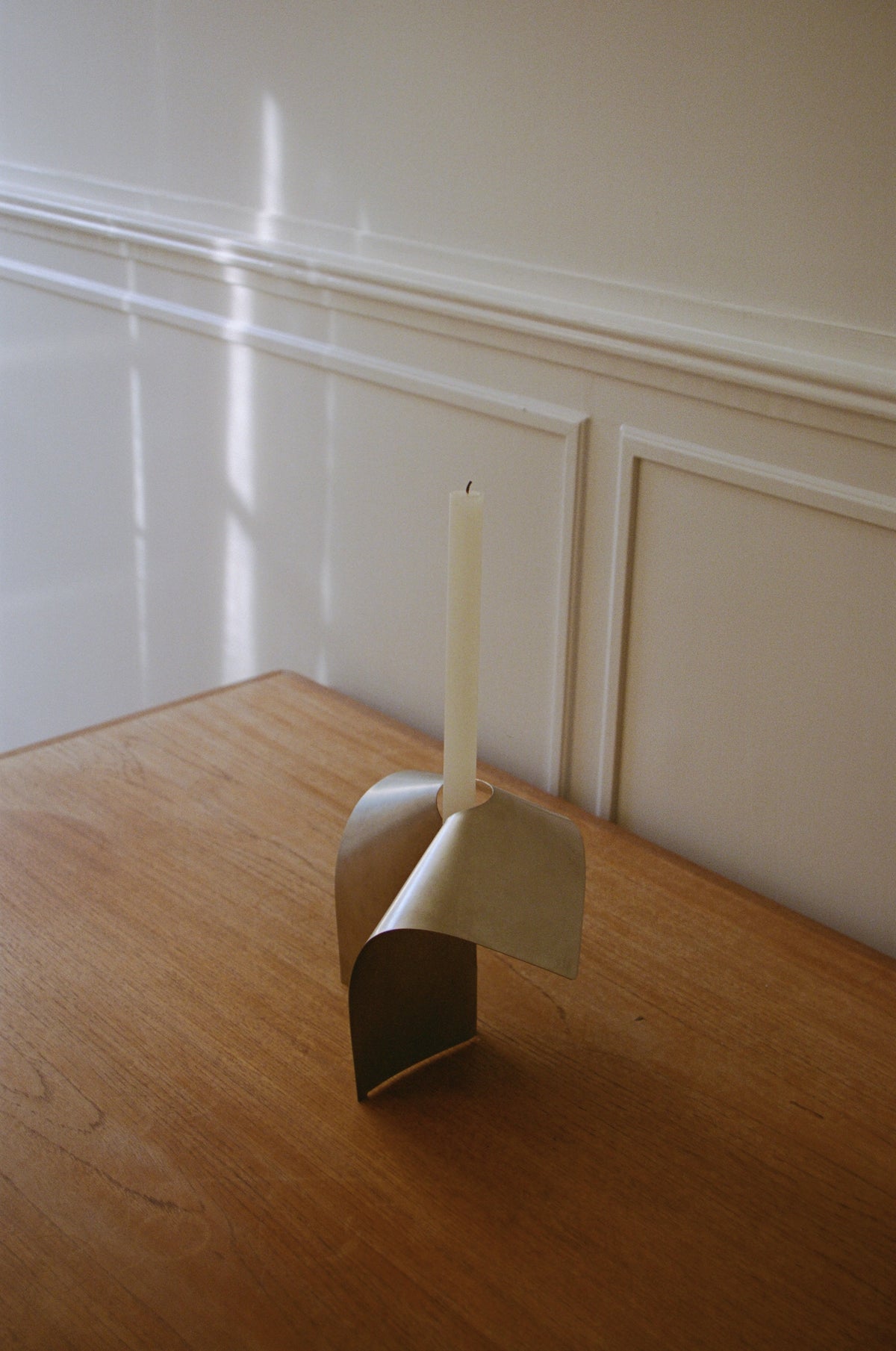 Stainless steel candle holder with a minimal bent shape, featuring a tall taper candle, handcrafted with precision, designed by Paul Coenen.