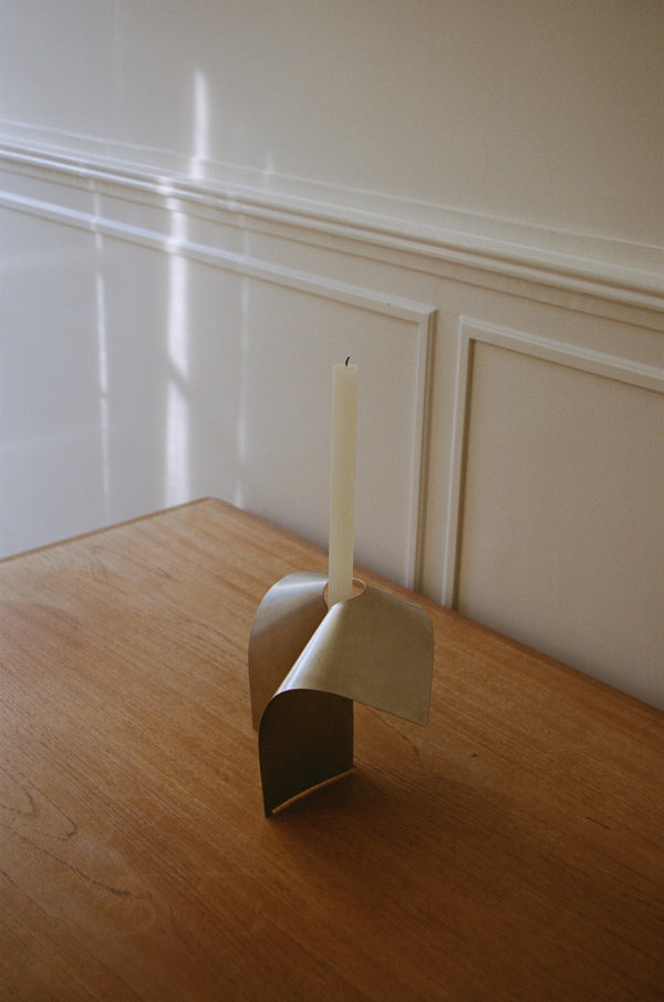 Stainless steel candle holder with a minimal bent shape, featuring a tall taper candle, handcrafted with precision, designed by Paul Coenen.