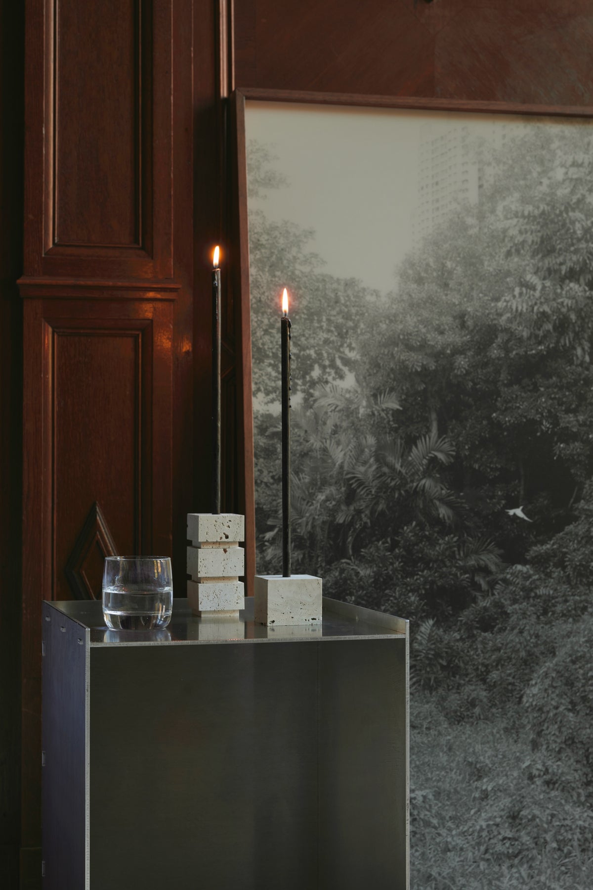 Sculptural candle holder small | travertine with two tall black candles, set on a metal table, handcrafted from Italian travertine by Dutch artist Louis Crombag.