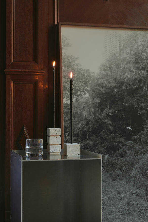 Sculptural candle holder small | travertine with two tall black candles, set on a metal table, handcrafted from Italian travertine by Dutch artist Louis Crombag.