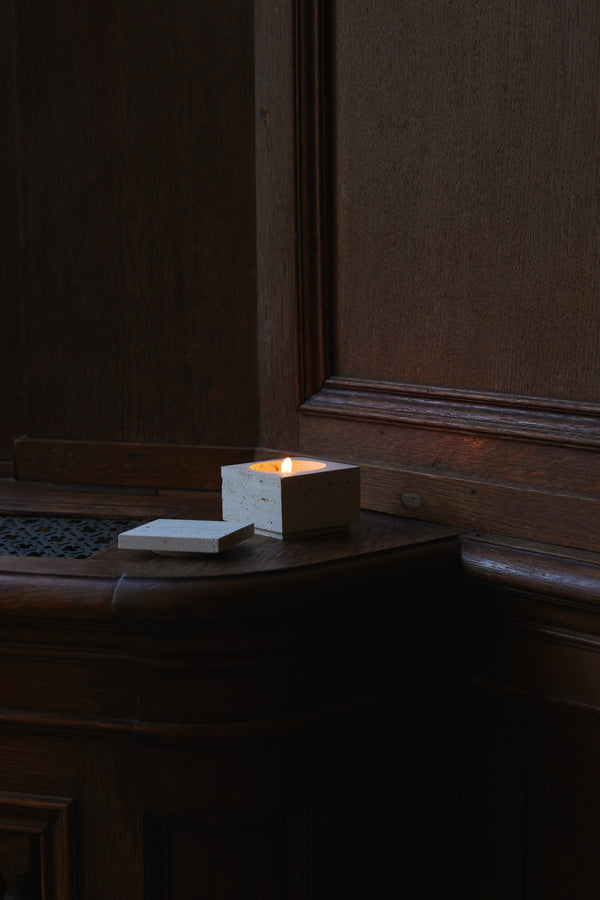 Tealight box | travertine: A handcrafted square stone container with lid, holding a lit candle, set on a dark wooden surface, highlighting its artisanal charm.