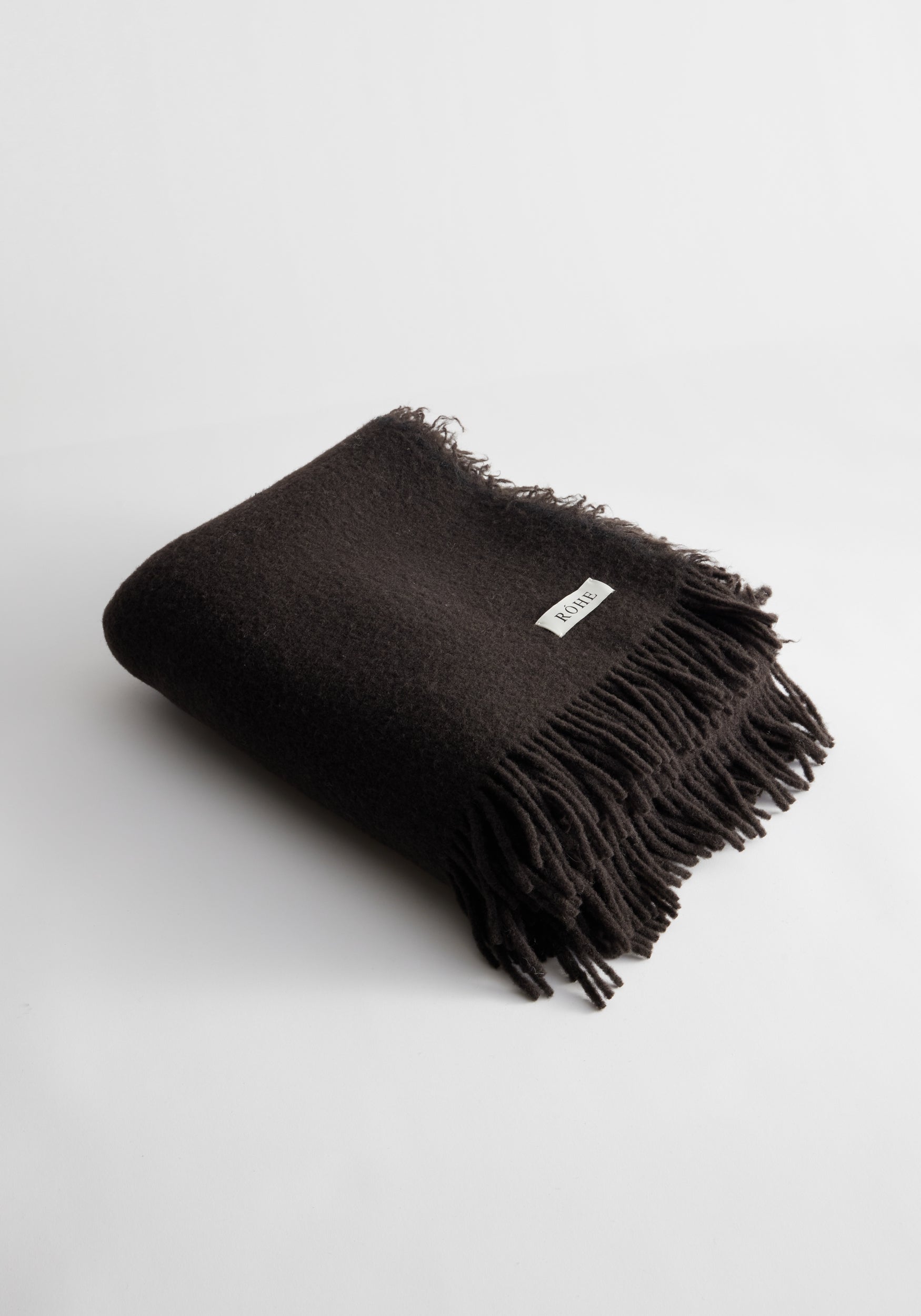 Folded wool blanket | chocolate color with fringed edges and a small white label on a plain white background.