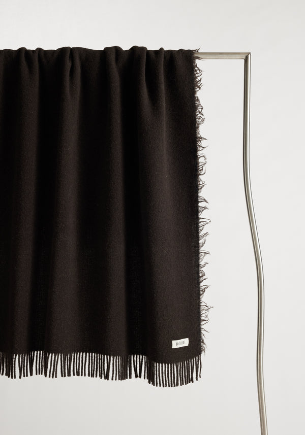 Wool blanket | chocolate: Italian-made brushed wool blanket with chunky fringes, draped over a metal stand, featuring a woven “RŌHE” label.