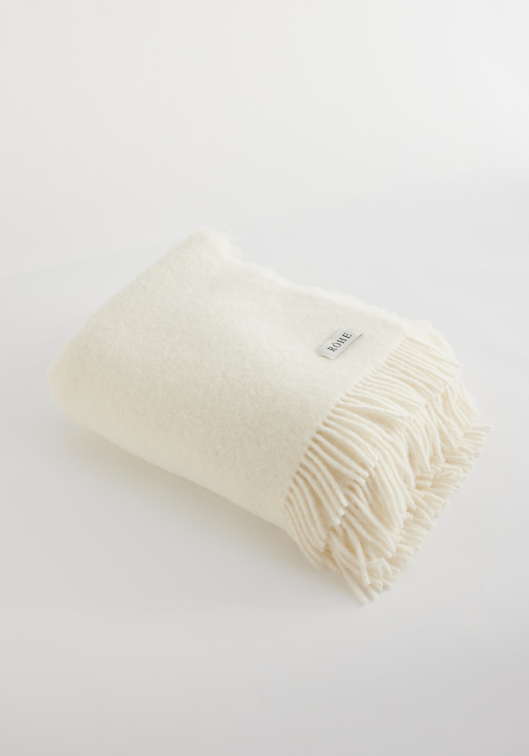 Soft cream-colored wool blanket | Cream neatly folded with fringe edges on a light background, showcasing cozy texture and subtle woven label detail.