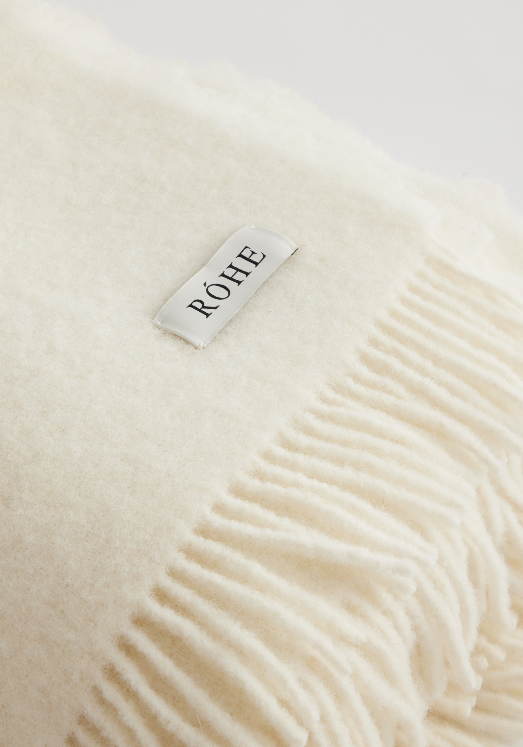 Close-up of a soft cream wool blanket with fringe detailing and a small brand tag, showcasing the texture and warmth of the Wool blanket | Cream.