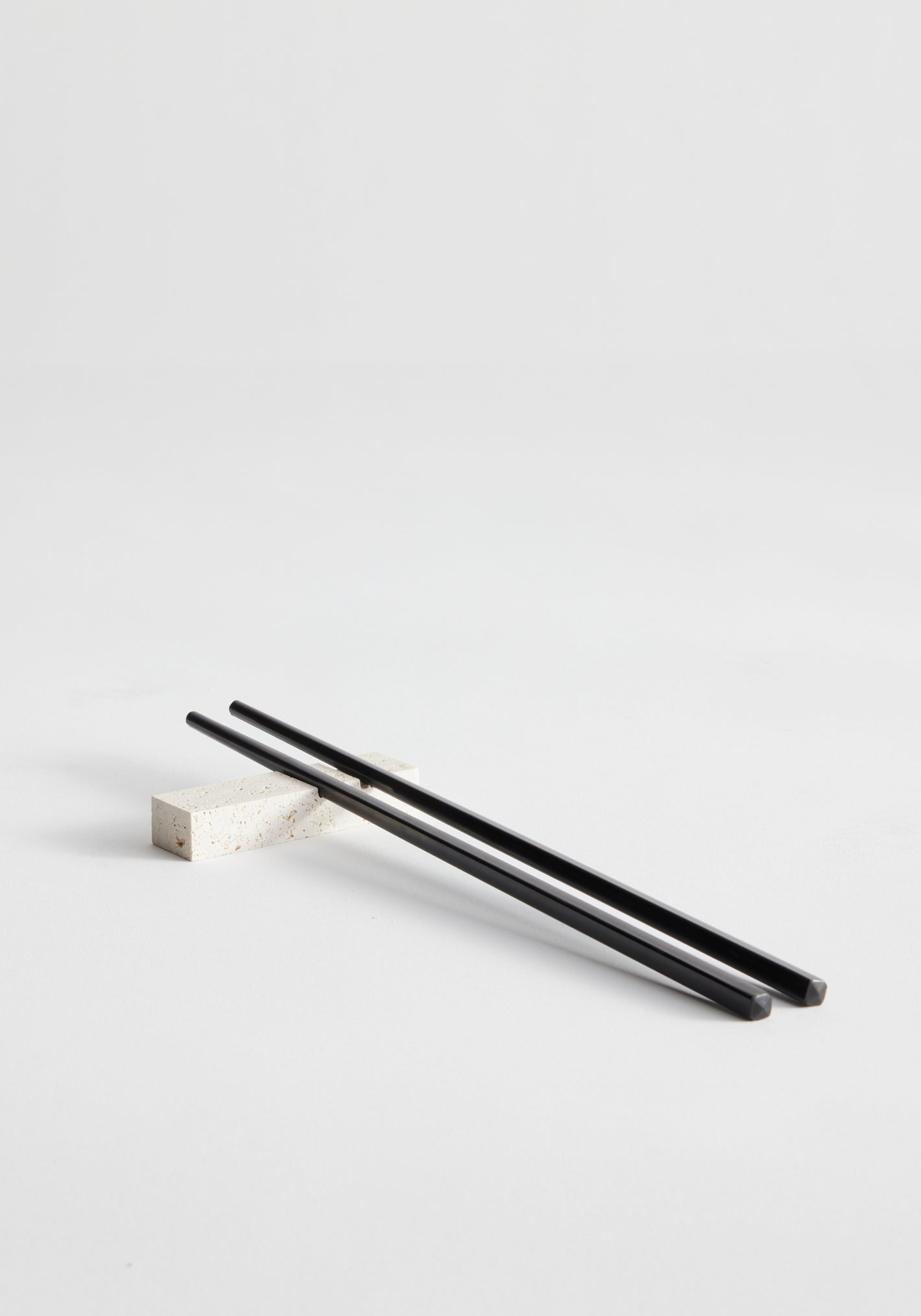 Chopstick holders | travertine: Black chopsticks rest on a handcrafted travertine chopstick holder by Louis Crombag, showcasing unique craftsmanship from leftover Italian stone.