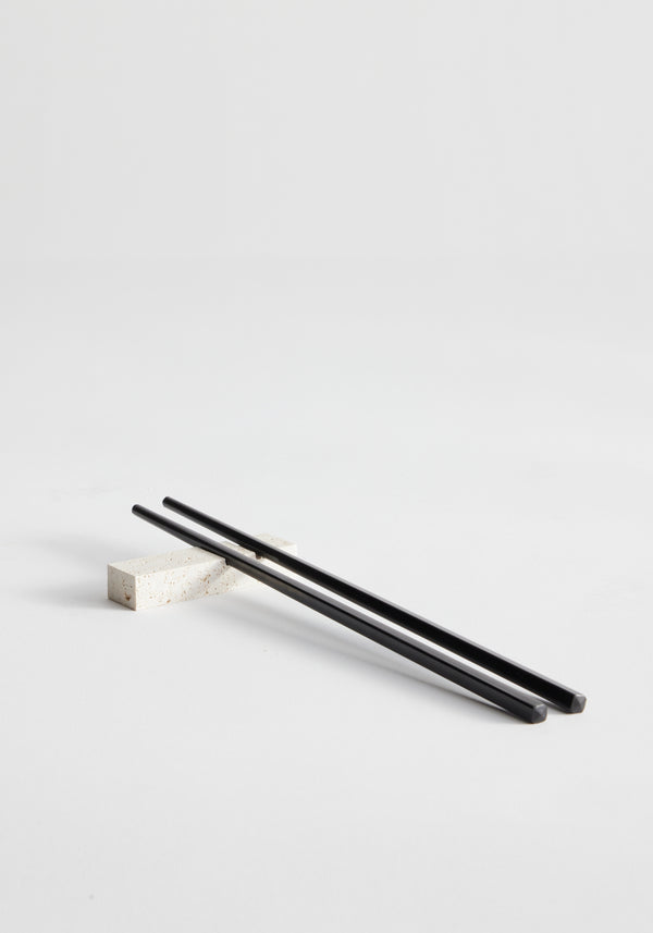 Chopstick holders | travertine: Black chopsticks rest on a handcrafted travertine chopstick holder by Louis Crombag, showcasing unique craftsmanship from leftover Italian stone.