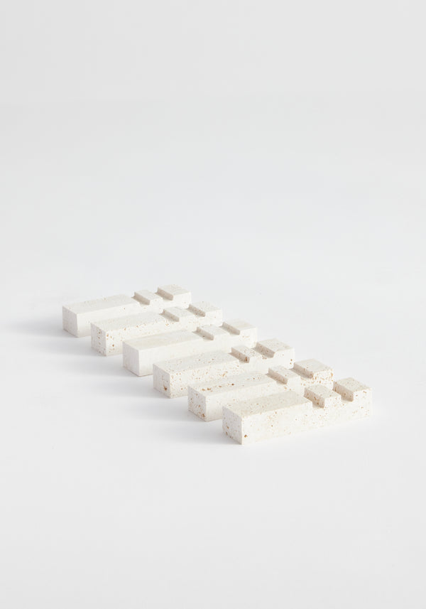Chopstick holders | travertine: A minimalist set of six white travertine blocks, handcrafted with stepped ends, arranged in offset rows on a monochromatic surface.