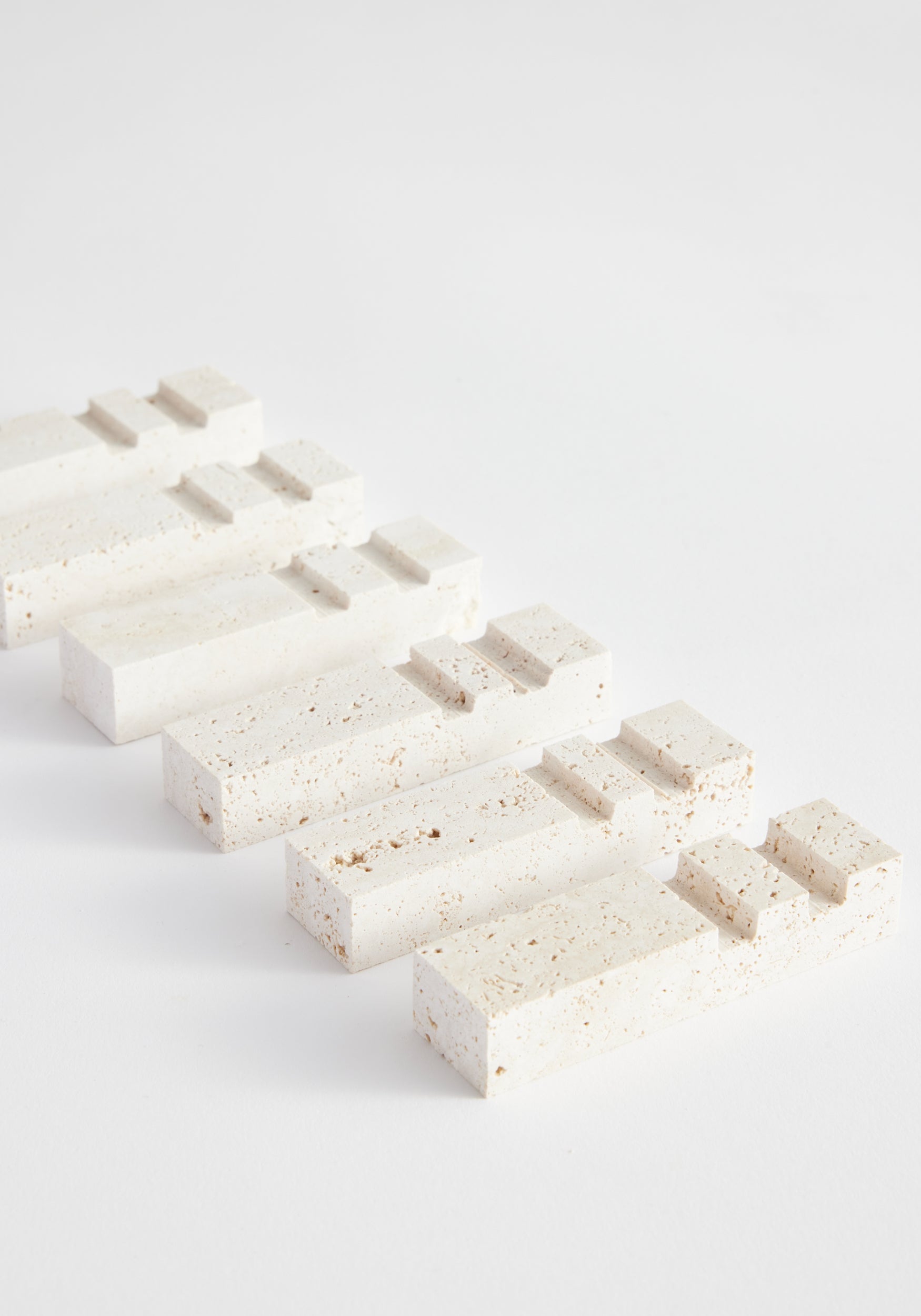 Five rectangular chopstick holders | travertine arranged in a diagonal line on a white surface, showcasing their natural porous texture and minimalist design.