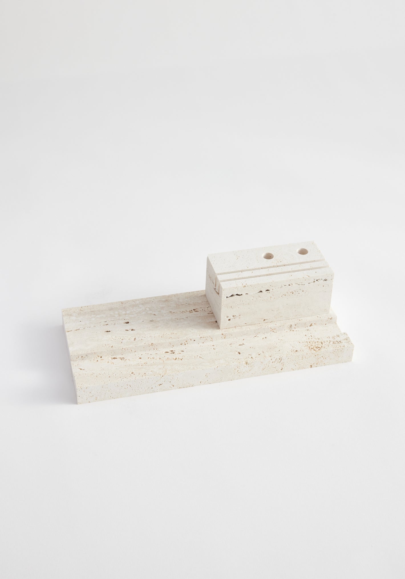 Desk organizer | travertine: Minimal two-piece stone set featuring a rectangular slab and a grooved, hole-pierced block, handcrafted from Italian travertine by artist Louis Crombag.