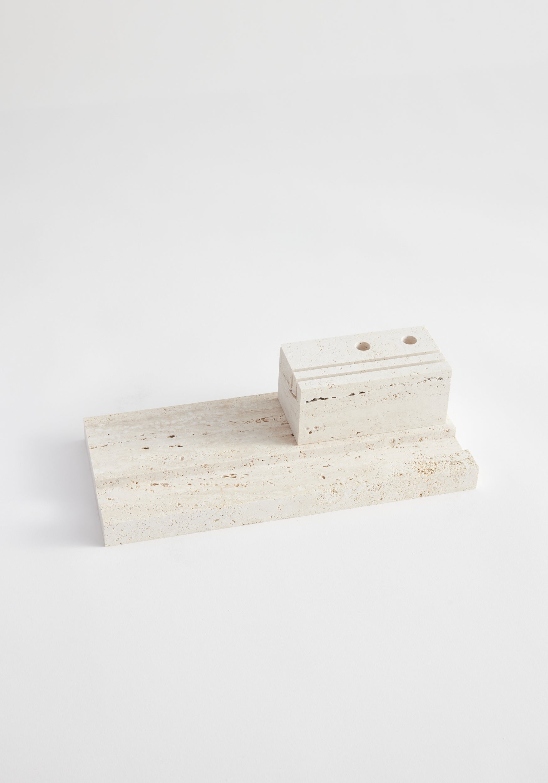Desk organizer | travertine: Minimal two-piece stone set featuring a rectangular slab and a grooved, hole-pierced block, handcrafted from Italian travertine by artist Louis Crombag.