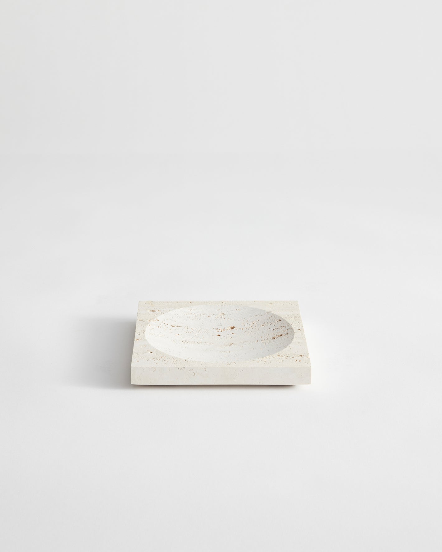 Small tray | travertine: A square stone tray with a central circular depression, handcrafted from speckled travertine, measuring 16cm by 16cm, designed by Louis Crombag.