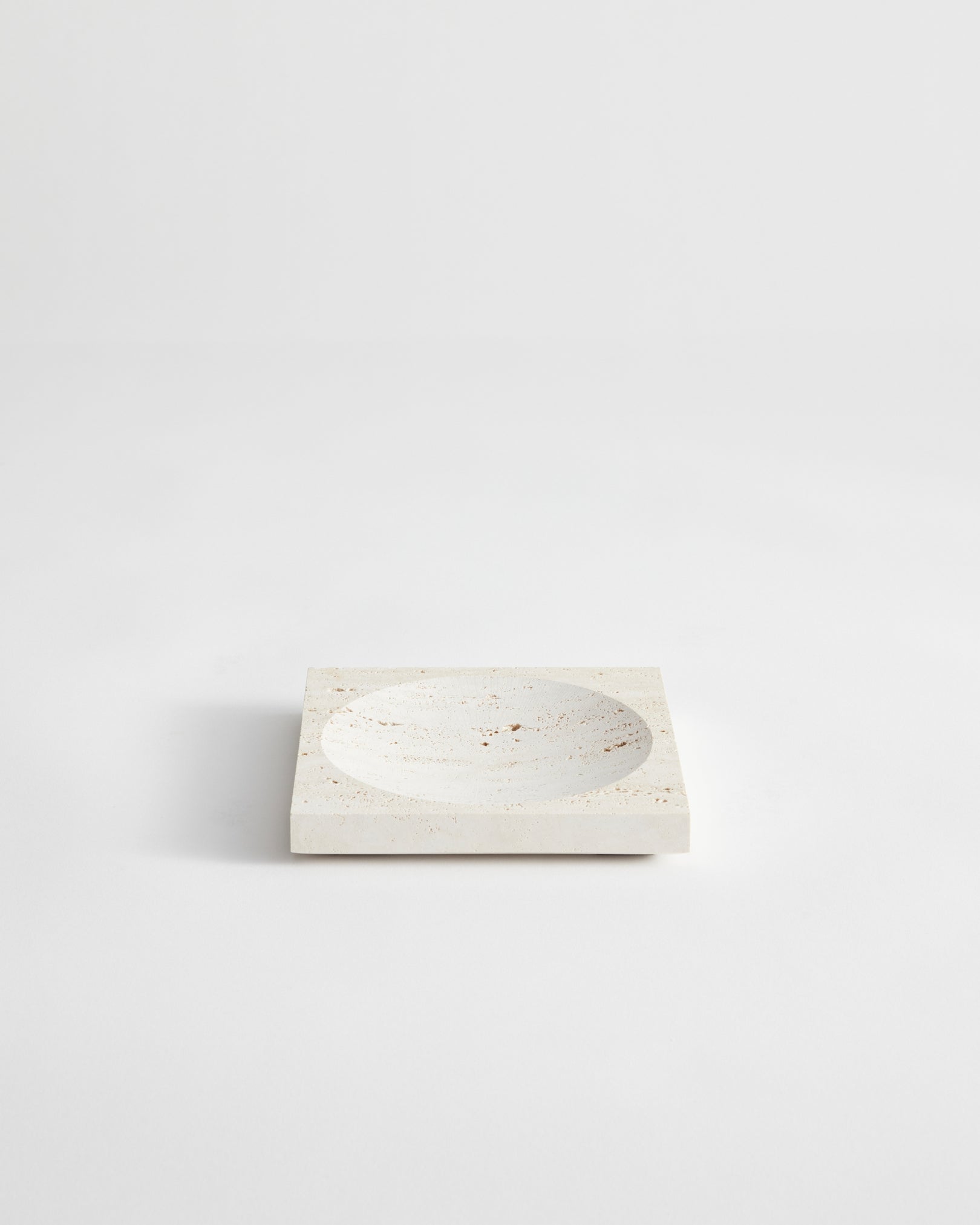Small tray | travertine: A square stone tray with a central circular depression, handcrafted from speckled travertine, measuring 16cm by 16cm, designed by Louis Crombag.