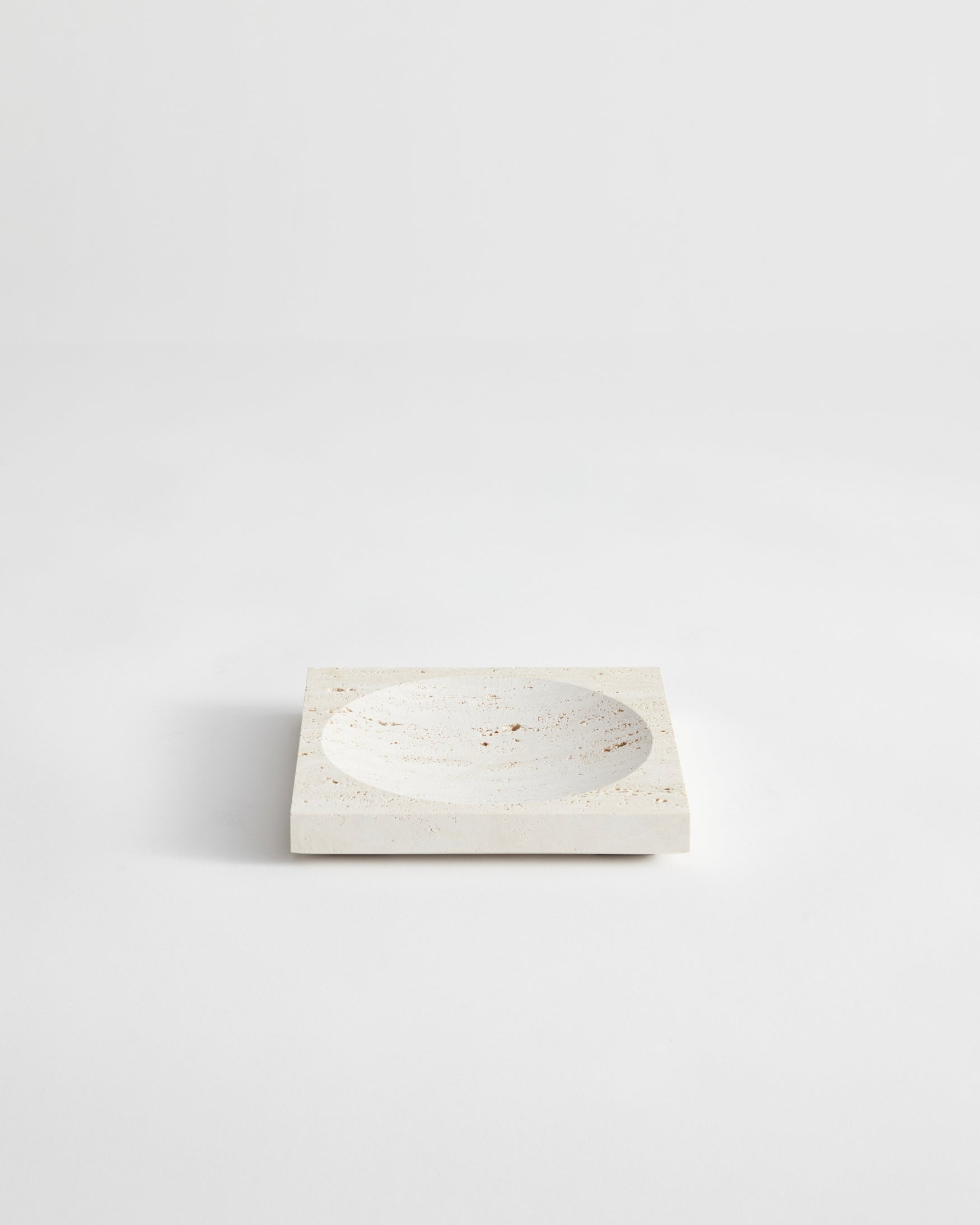 Small tray | travertine: A square stone tray with a central circular depression, handcrafted from speckled travertine, measuring 16cm by 16cm, designed by Louis Crombag.