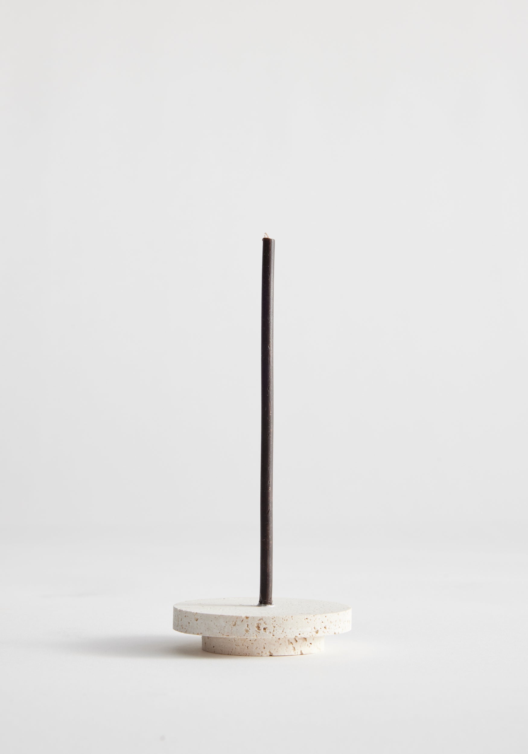 Dish candleholder small | travertine: A single black incense stick stands in a handcrafted round travertine holder by Louis Crombag, showcasing unique craftsmanship.