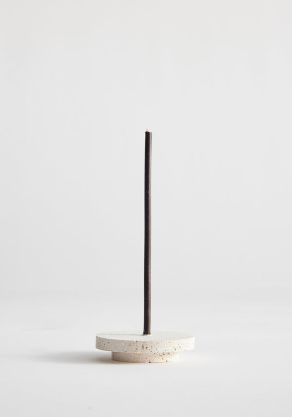 Dish candleholder small | travertine: A single black incense stick stands in a handcrafted round travertine holder by Louis Crombag, showcasing unique craftsmanship.