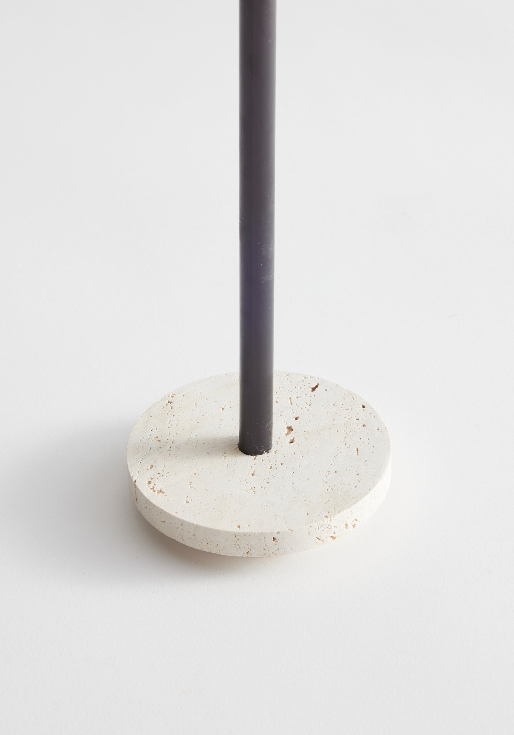 Dish candleholder small | travertine, featuring a minimalist design with a dark metal rod on a flat, handcrafted cream travertine base, includes two 5mm candles.