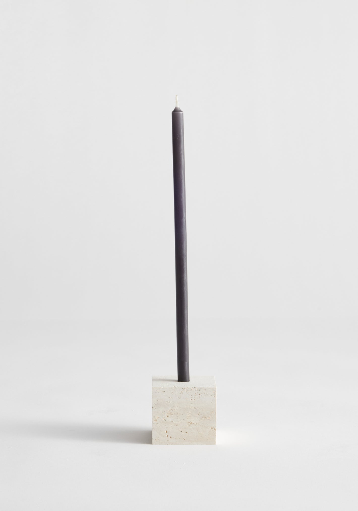 Two-way cube candleholder in travertine, showcasing a dark gray taper candle in a cube-shaped natural stone holder, handcrafted by Louis Crombag in the Netherlands.