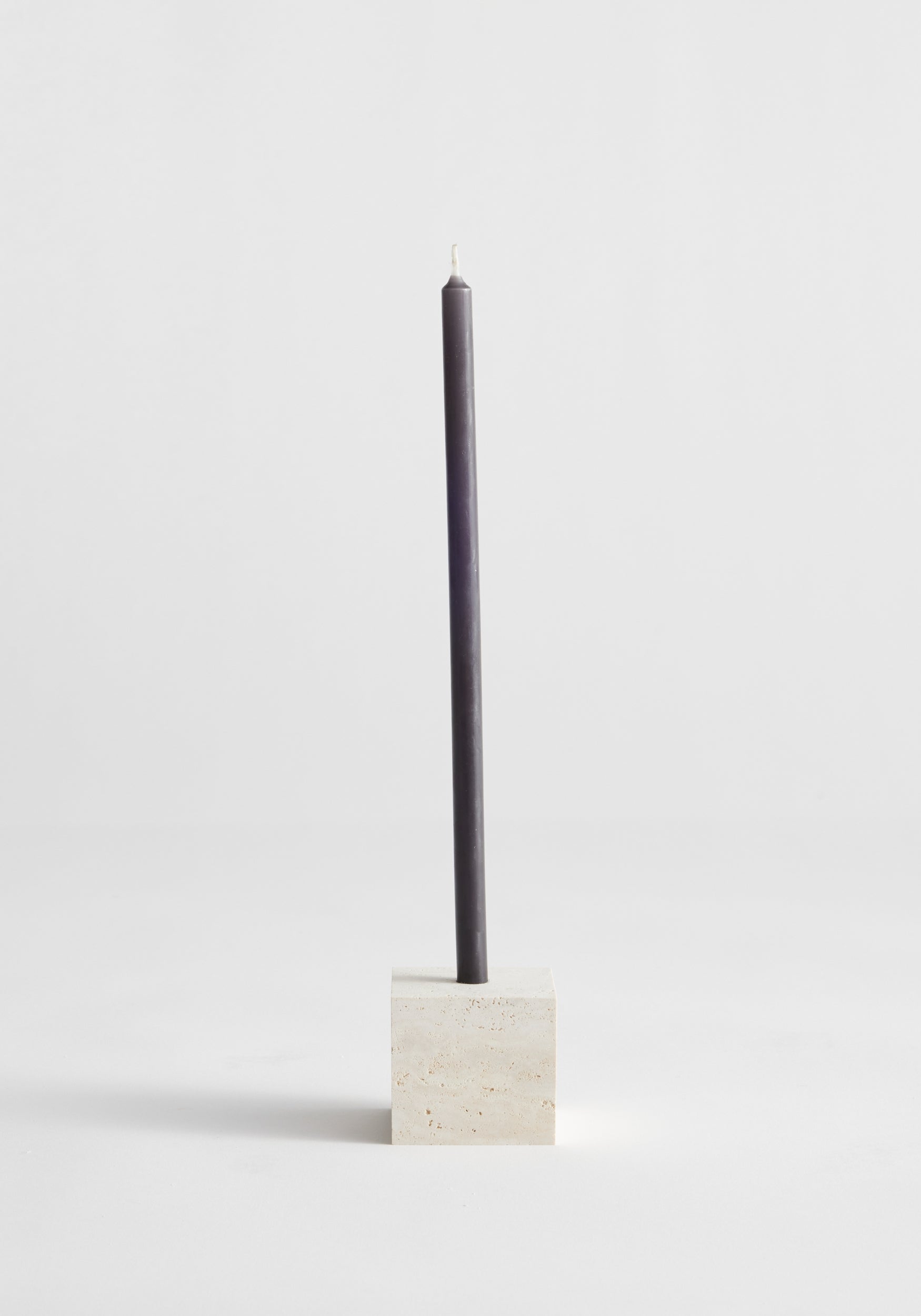 Two-way cube candleholder in travertine, showcasing a dark gray taper candle in a cube-shaped natural stone holder, handcrafted by Louis Crombag in the Netherlands.
