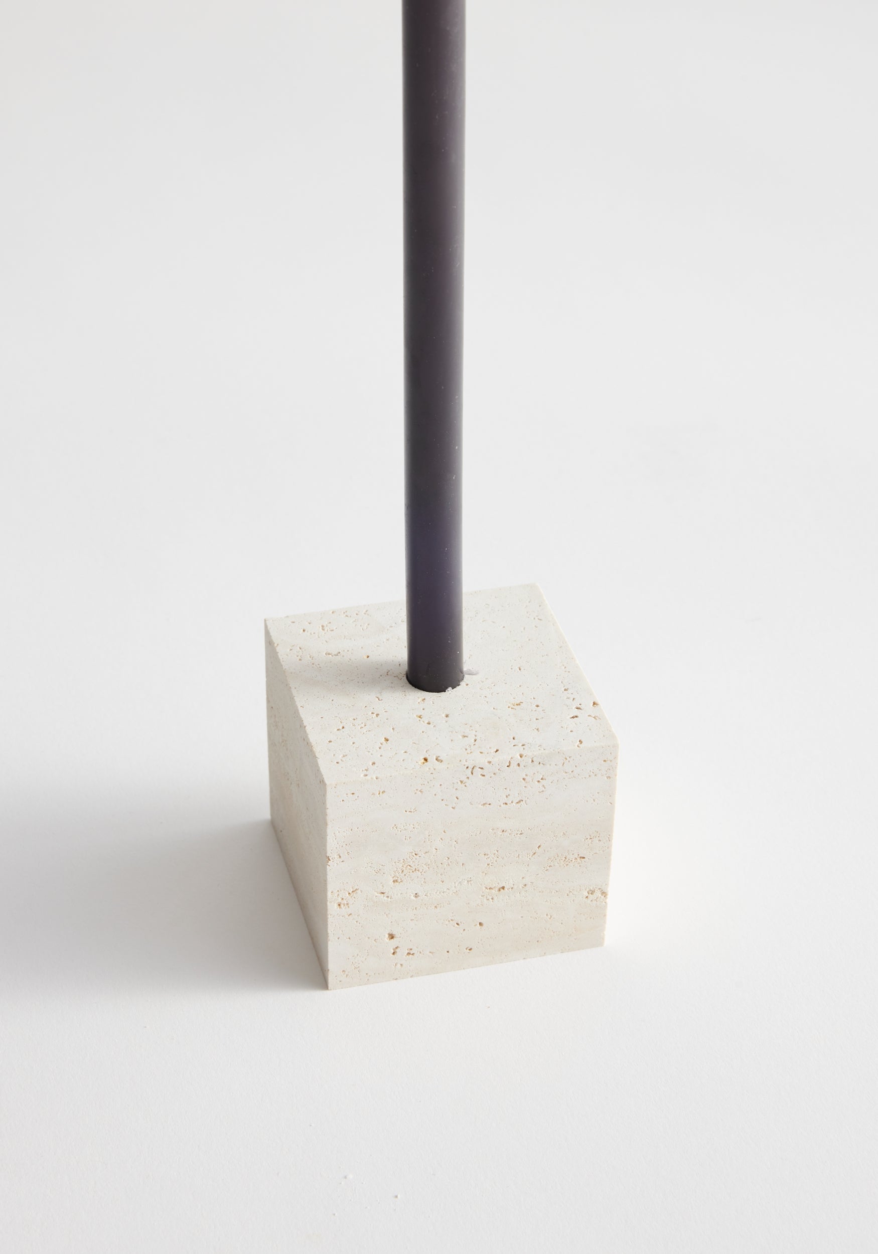 Two-way cube candleholder made of travertine with a dark taper candle inserted, showcasing its versatile design handcrafted by Louis Crombag in the Netherlands.