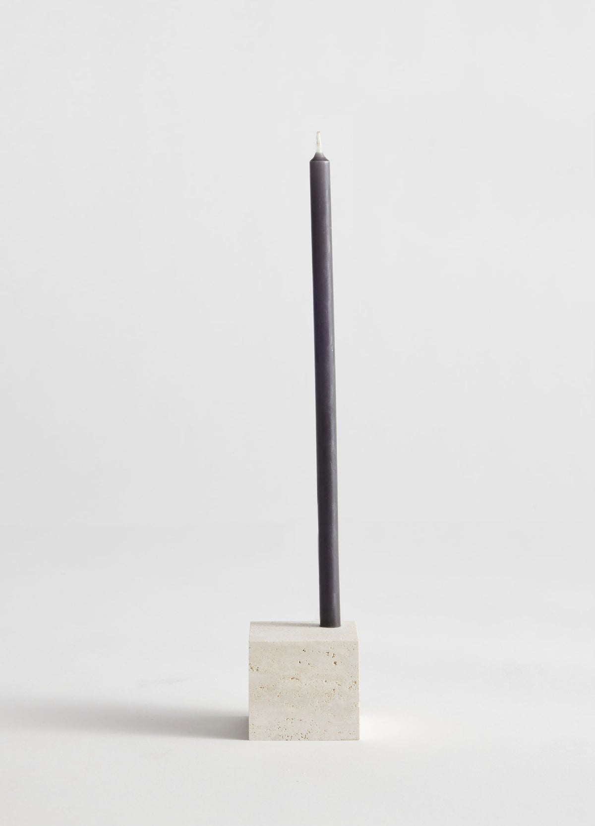 Two-way cube candleholder | travertine, featuring a dark gray taper candle in a handcrafted, cubical travertine holder by Dutch artist Louis Crombag.
