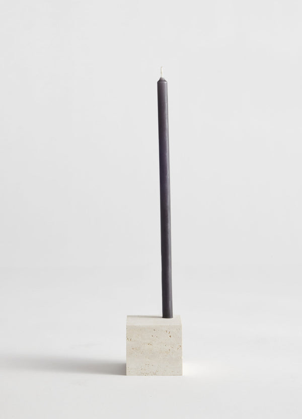 Two-way cube candleholder | travertine, featuring a dark gray taper candle in a handcrafted, cubical travertine holder by Dutch artist Louis Crombag.
