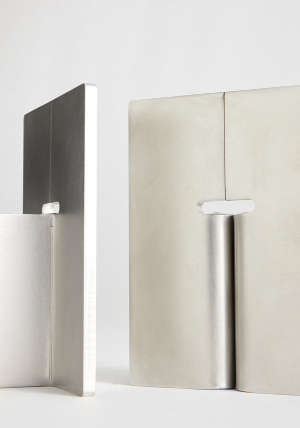 Stainless steel bookends featuring L-shaped design with a hinged variant, handcrafted from 8mm stainless steel, showcasing minimalist style by designer Paul Coenen.