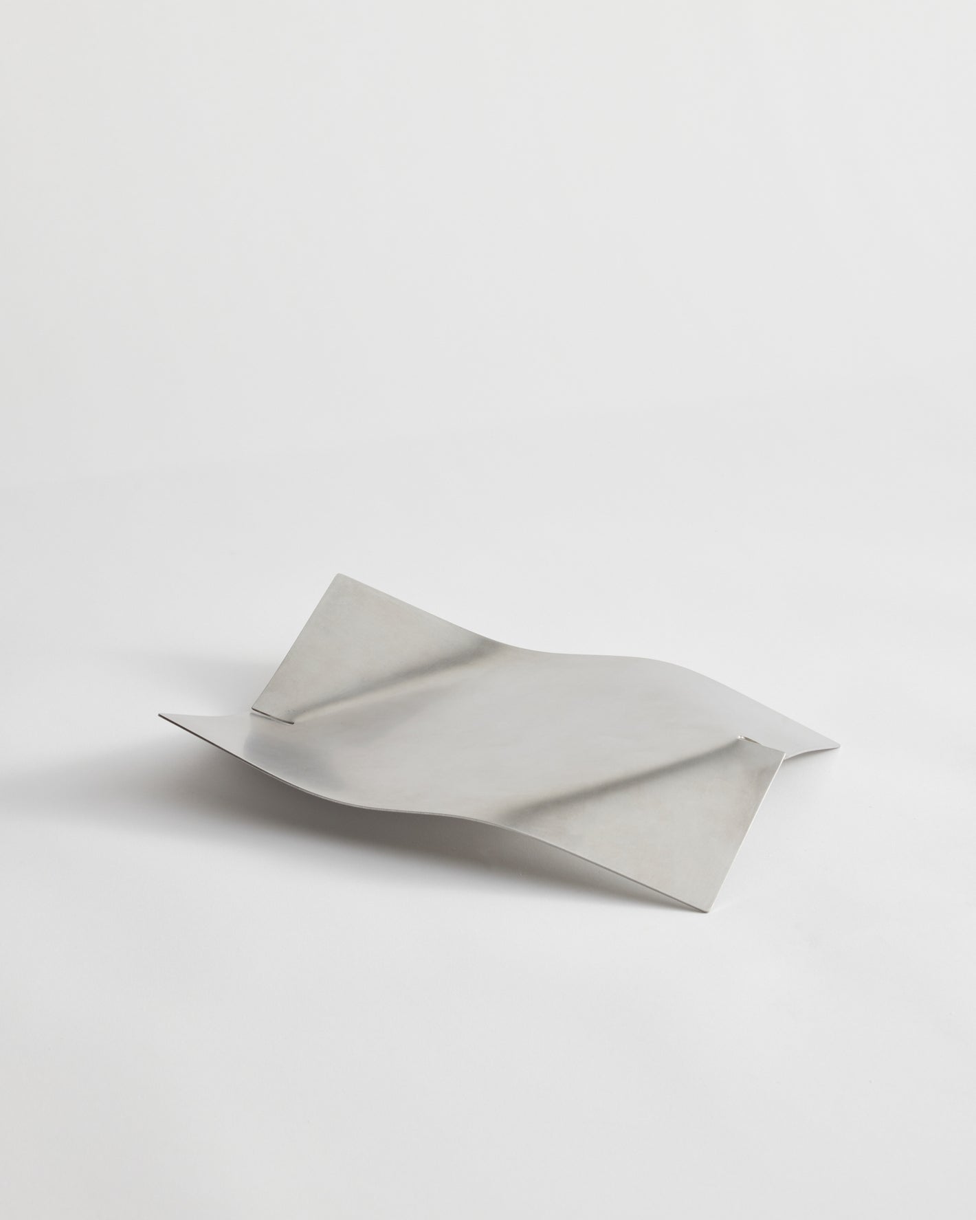 Stainless steel bowl with minimalist design, featuring gently bent ends for a tray-like shape. Handcrafted in the Netherlands, measuring 32cm x 23.5cm x 5.5cm.