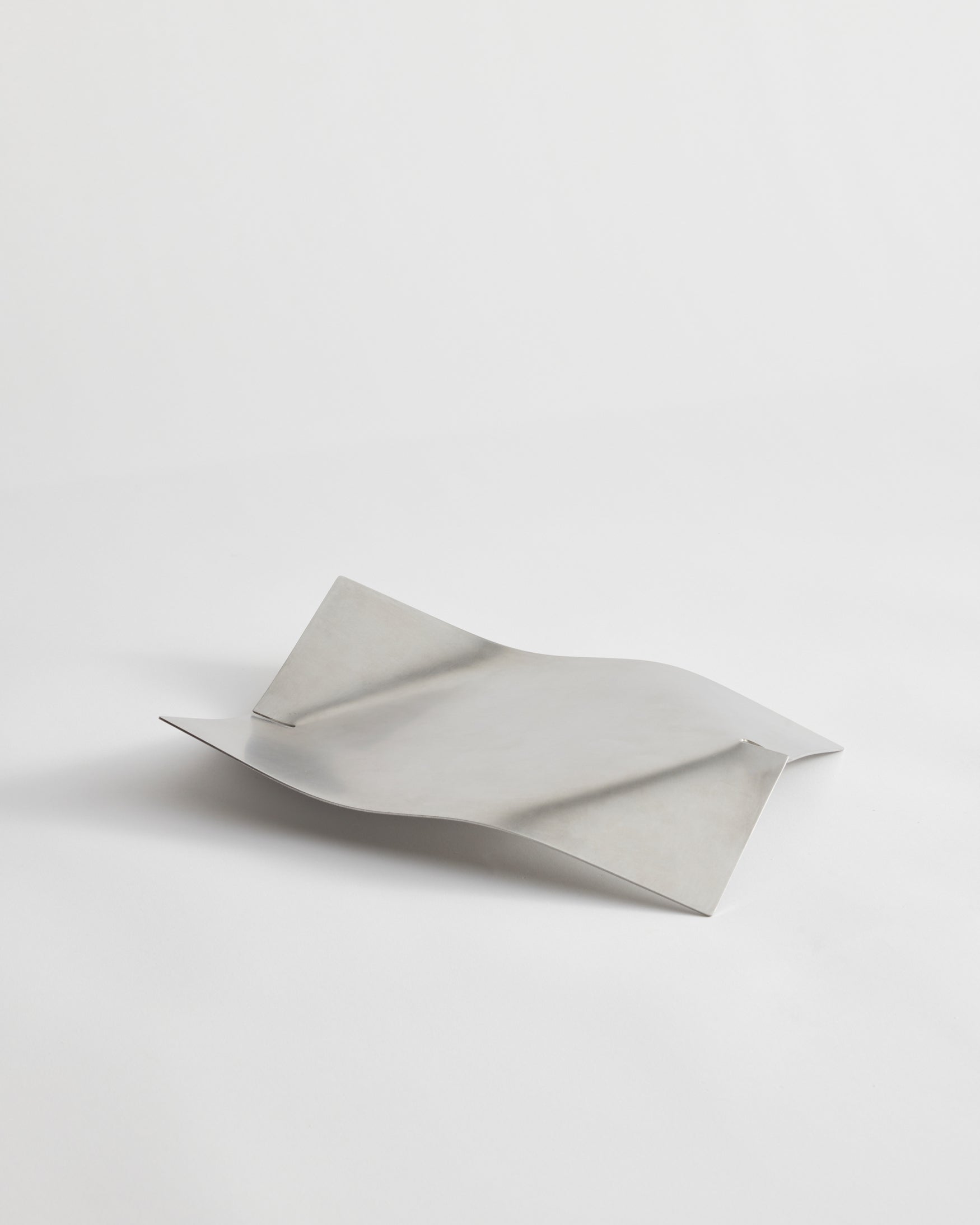 Stainless steel bowl with minimalist design, featuring gently bent ends for a tray-like shape. Handcrafted in the Netherlands, measuring 32cm x 23.5cm x 5.5cm.