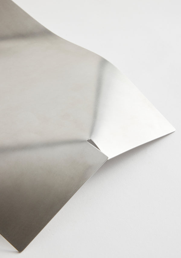 Stainless steel bowl in a minimal, bent shape, showcasing a smooth, reflective surface, handcrafted from a single notched sheet by Dutch designer Paul Coenen.