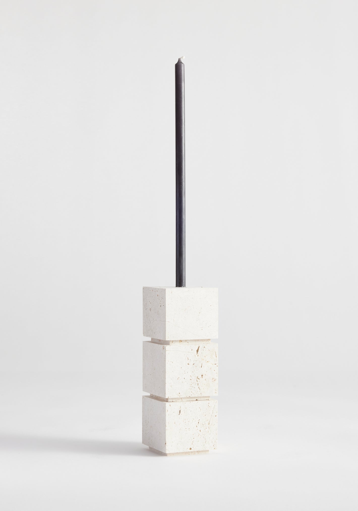 Sculptural candle holder small in travertine, featuring a black taper candle atop three white cubic stone blocks, handcrafted by Louis Crombag in the Netherlands.