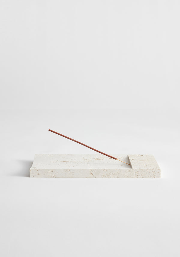 Incense holder tray | travertine: Slender incense stick rests on a handcrafted cream-colored rectangular stone tray, made from leftover Italian travertine by Dutch artist Louis Crombag.
