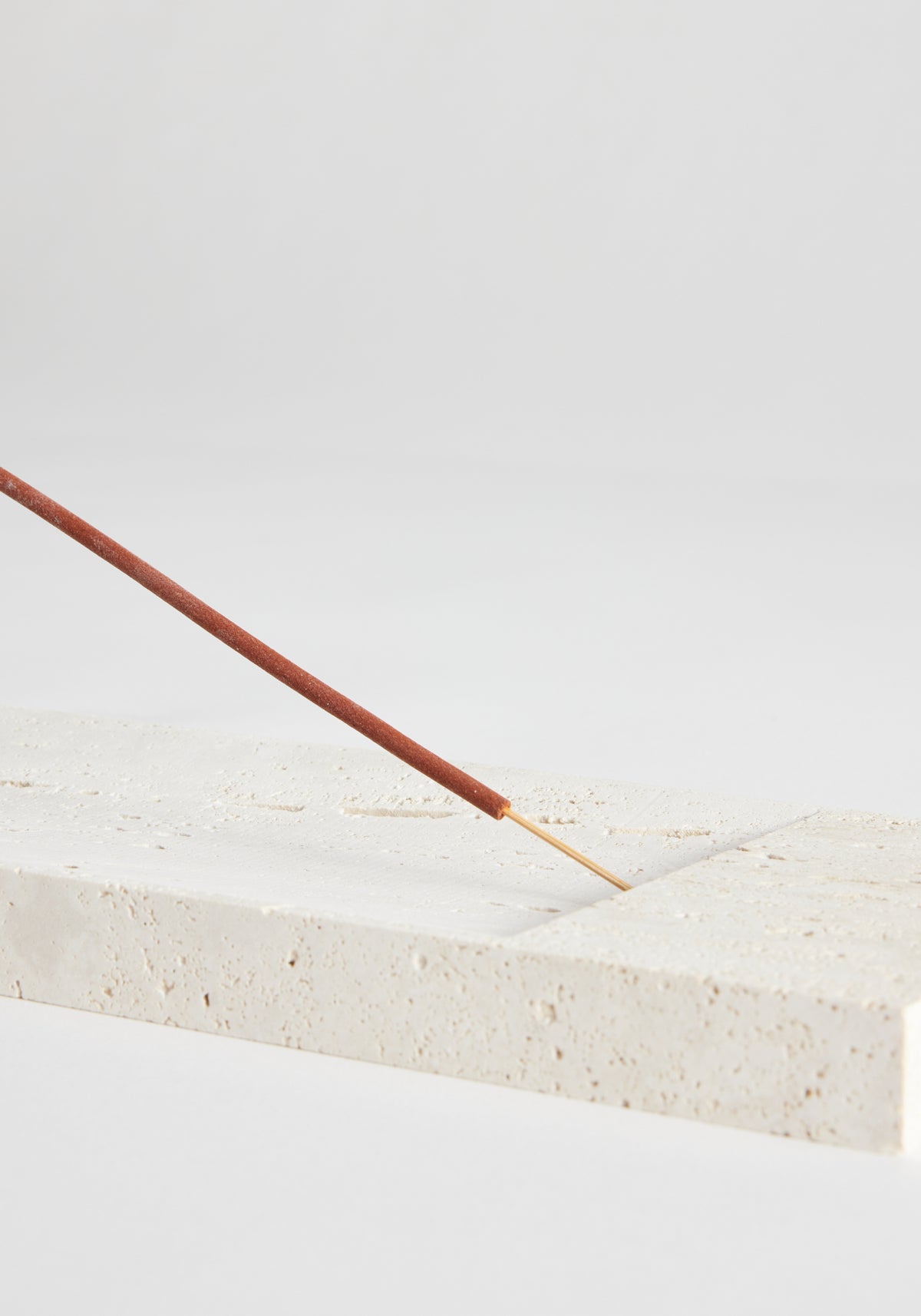 Incense holder tray in travertine, showcasing a slender incense stick on a handcrafted pale-beige block, designed by Louis Crombag in the Netherlands.