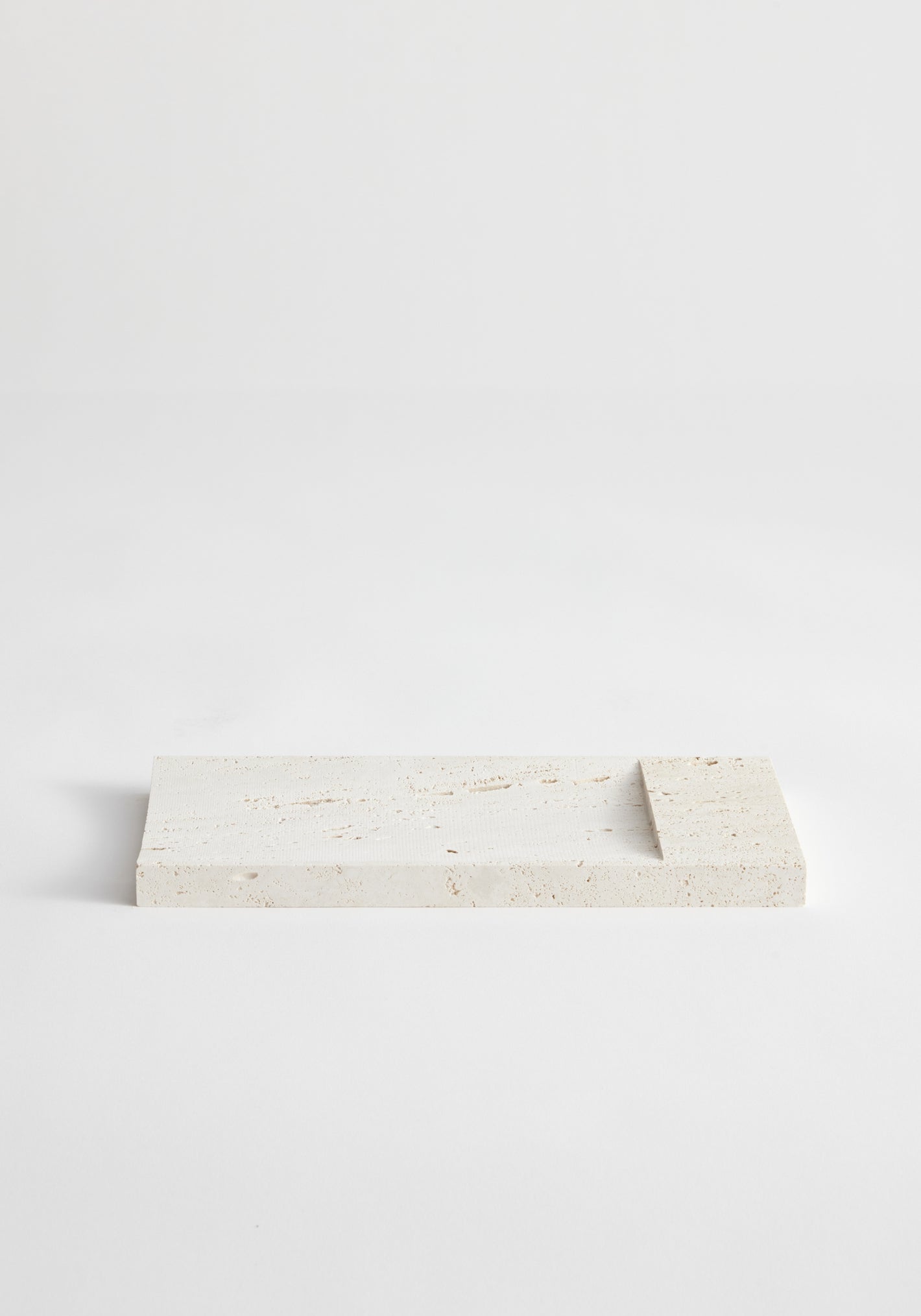 Incense holder tray | travertine: A handcrafted rectangular travertine slab with a raised edge, designed by Louis Crombag, serves as a minimalist incense holder.