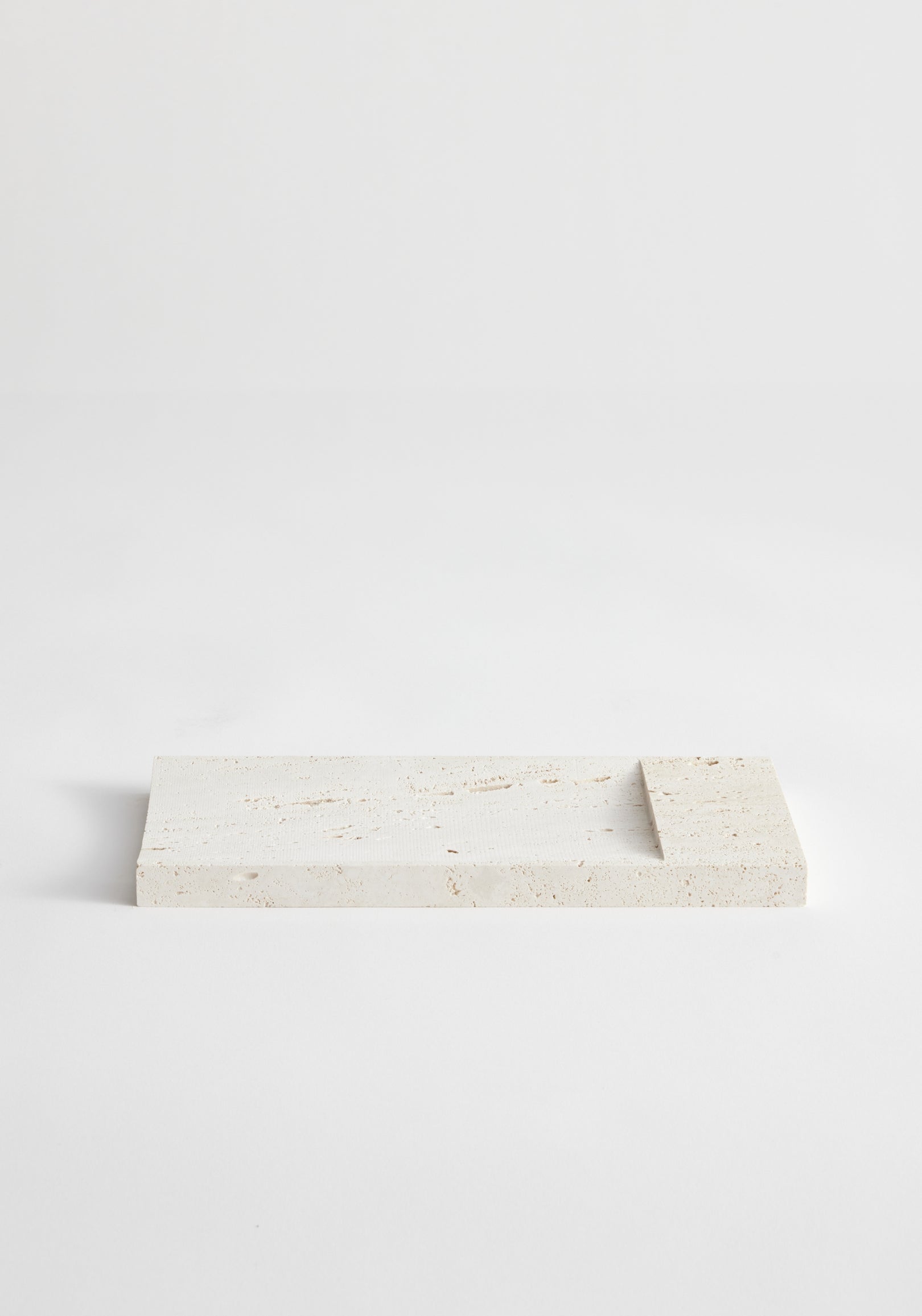 Incense holder tray | travertine: A handcrafted rectangular travertine slab with a raised edge, designed by Louis Crombag, serves as a minimalist incense holder.
