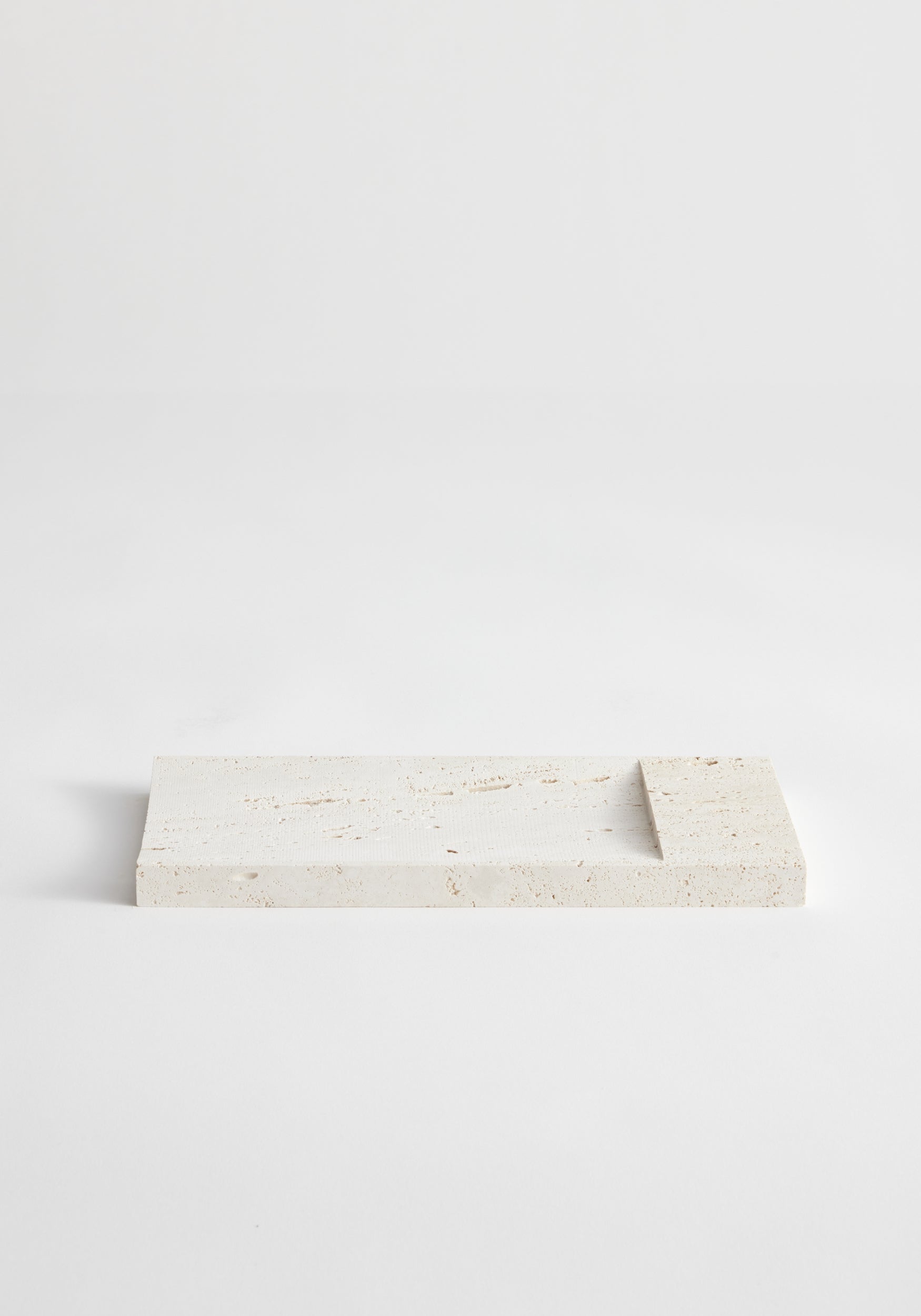 Incense holder tray | travertine: A handcrafted rectangular travertine slab with a raised edge, designed by Louis Crombag, serves as a minimalist incense holder.