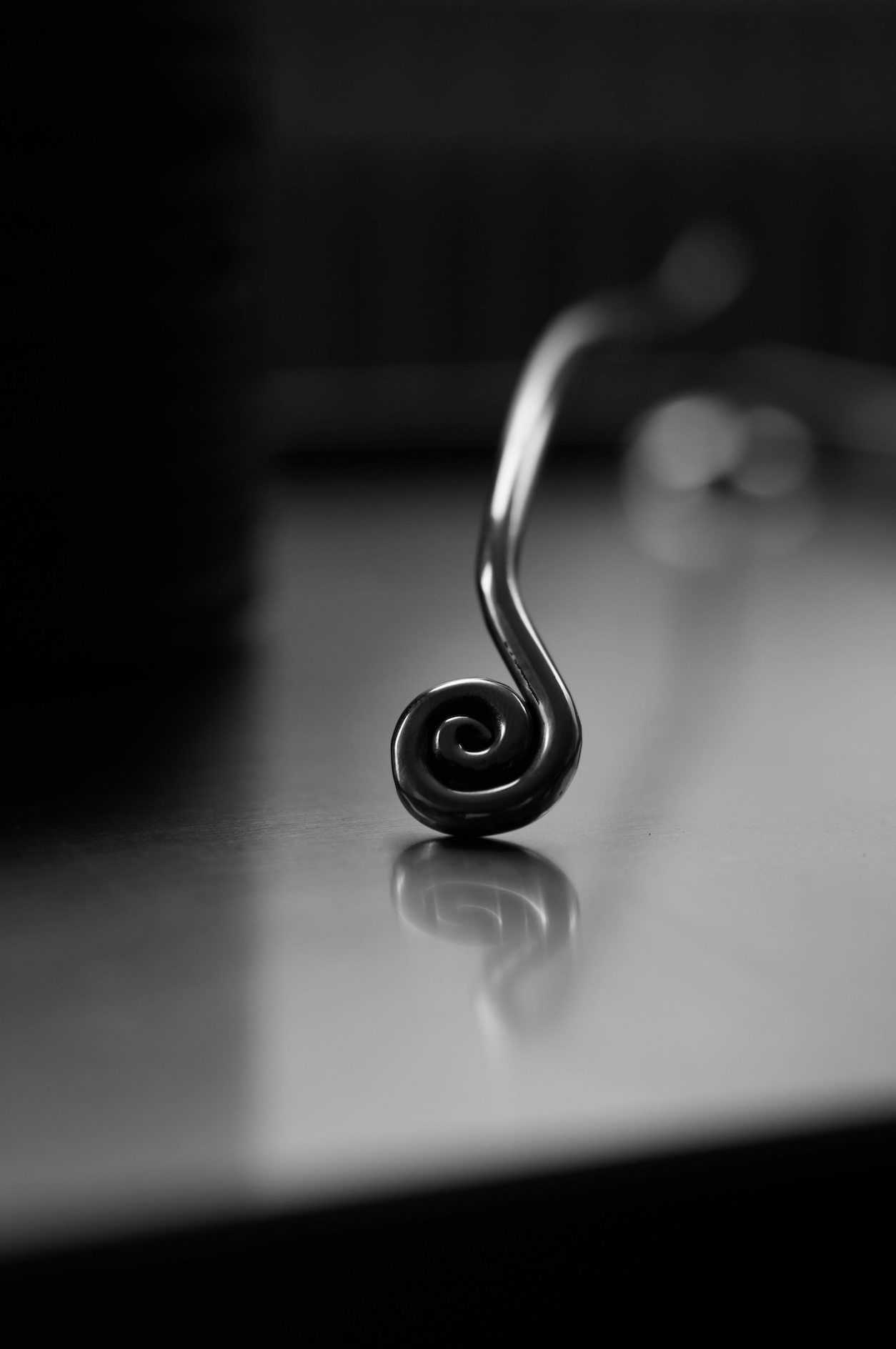 Candle Stopper | silver: A macro shot of a stainless steel candle snuffer with a coiled tip resting on a reflective surface, designed for safe candle extinguishing.