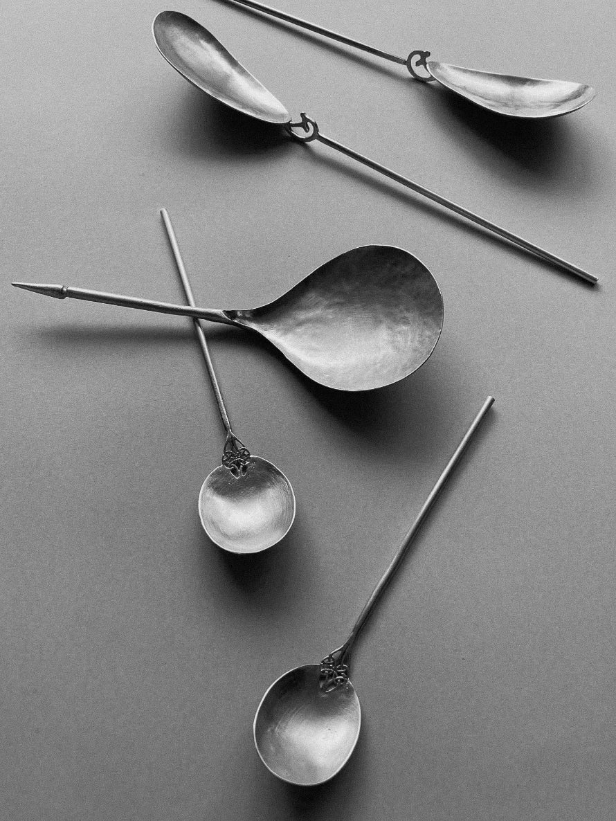 Set of vintage metal Tea Spoon utensils with long handles and rounded scoops, arranged on a gray background in a scattered pattern.