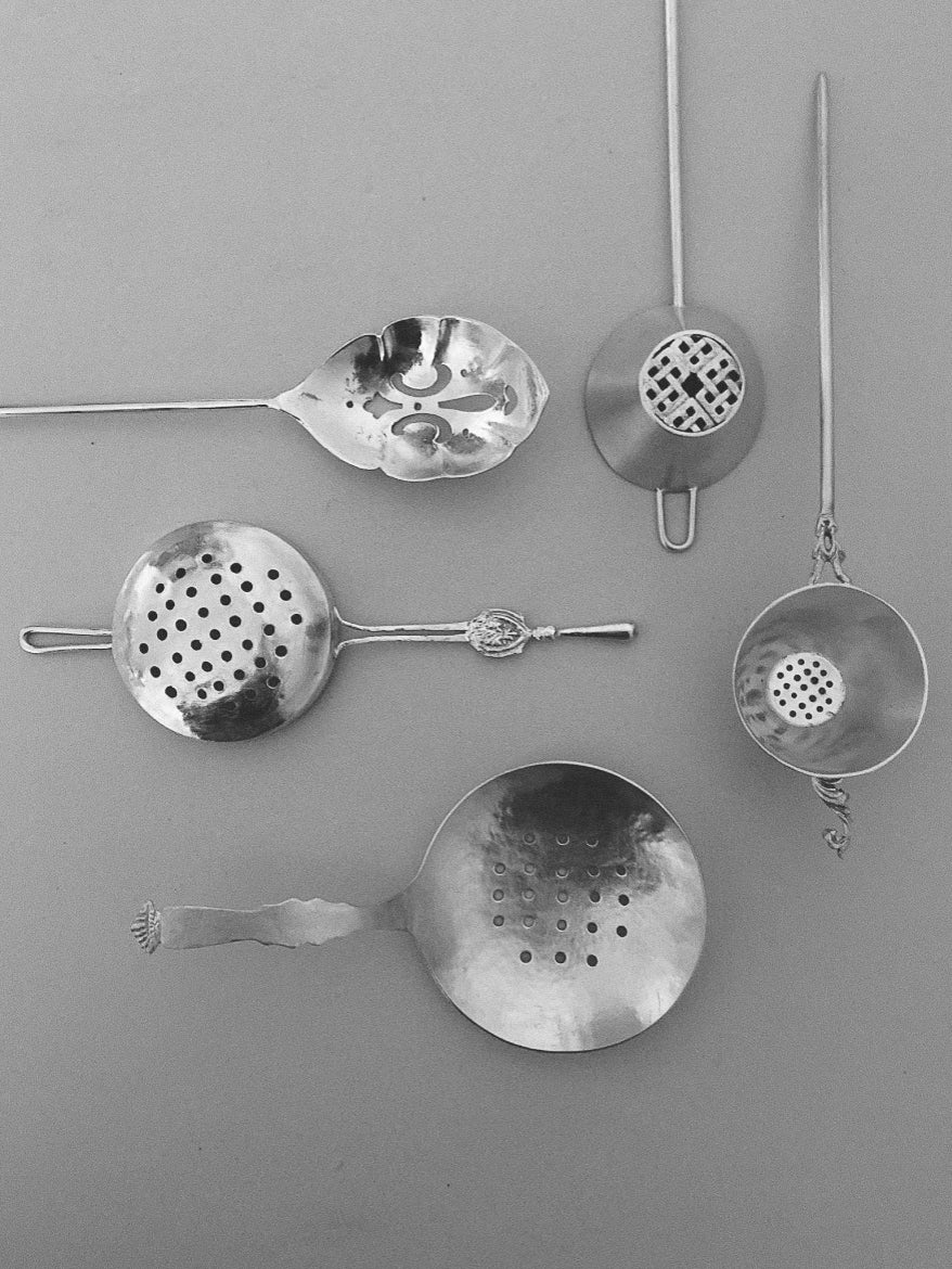 Collection of vintage metal Tea Strainer designs with varied perforations and intricate handles, arranged on a neutral background for display.