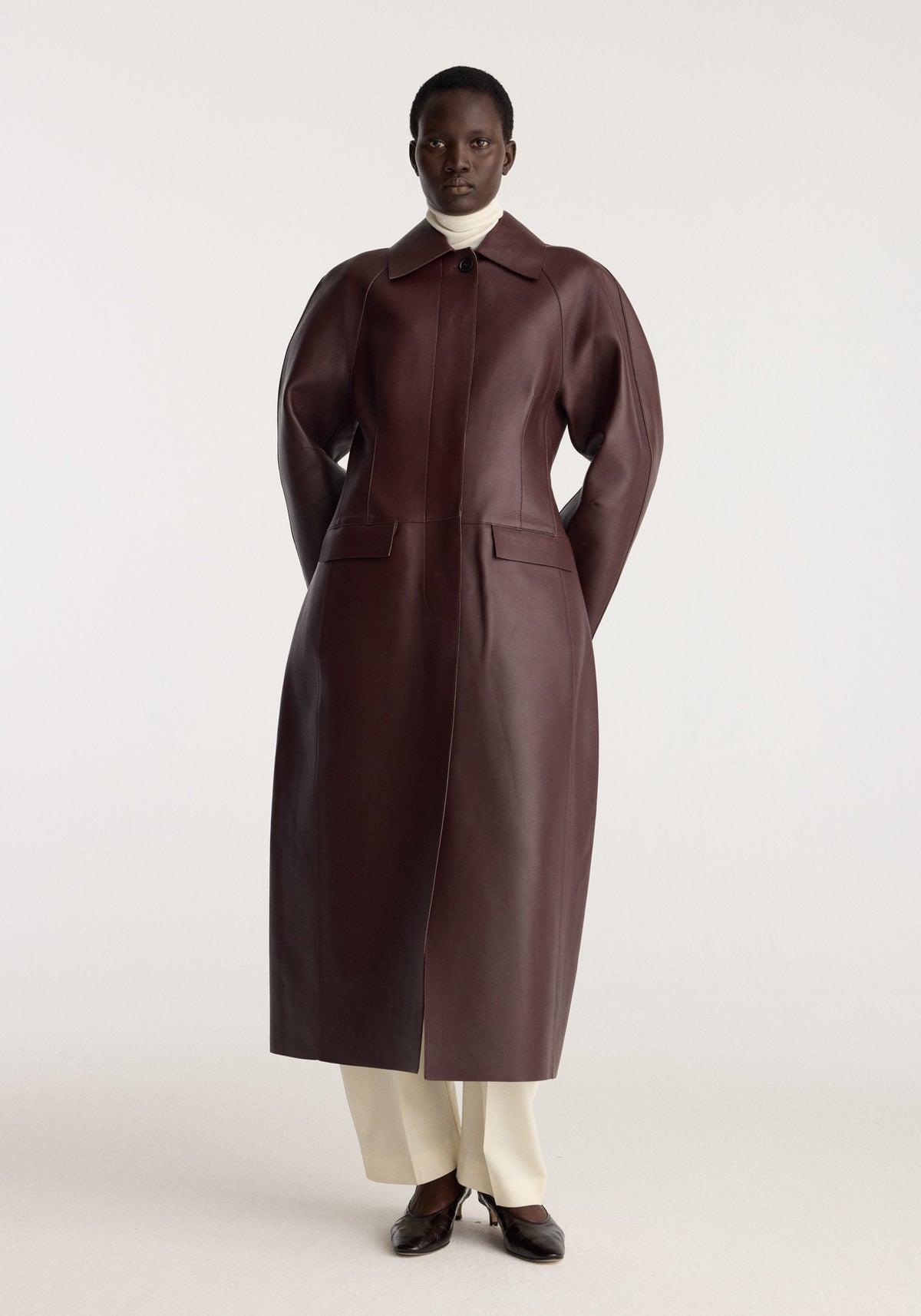 Sculptural Bonded Leather Coat | mahogany worn by a model with a structured silhouette pointed collar long sleeves front pockets and calf length hem