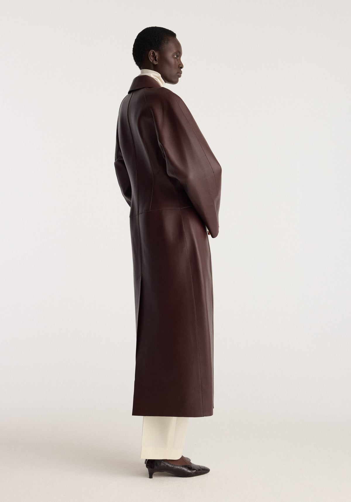 Sculptural Bonded Leather Coat | mahogany shown in side profile on a model with a long silhouette, oversized sleeves, and rich dark mahogany finish