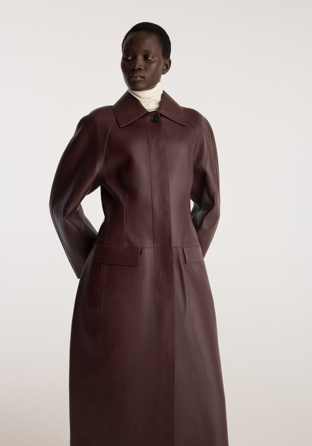Sculptural Bonded Leather Coat | mahogany worn by a model with a high collar long sleeves button front and front patch pockets in a studio setting