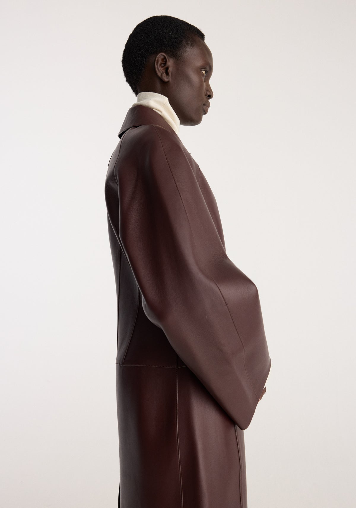Sculptural Bonded Leather Coat | mahogany shown in side profile on a model with a long relaxed silhouette and oversized sleeves